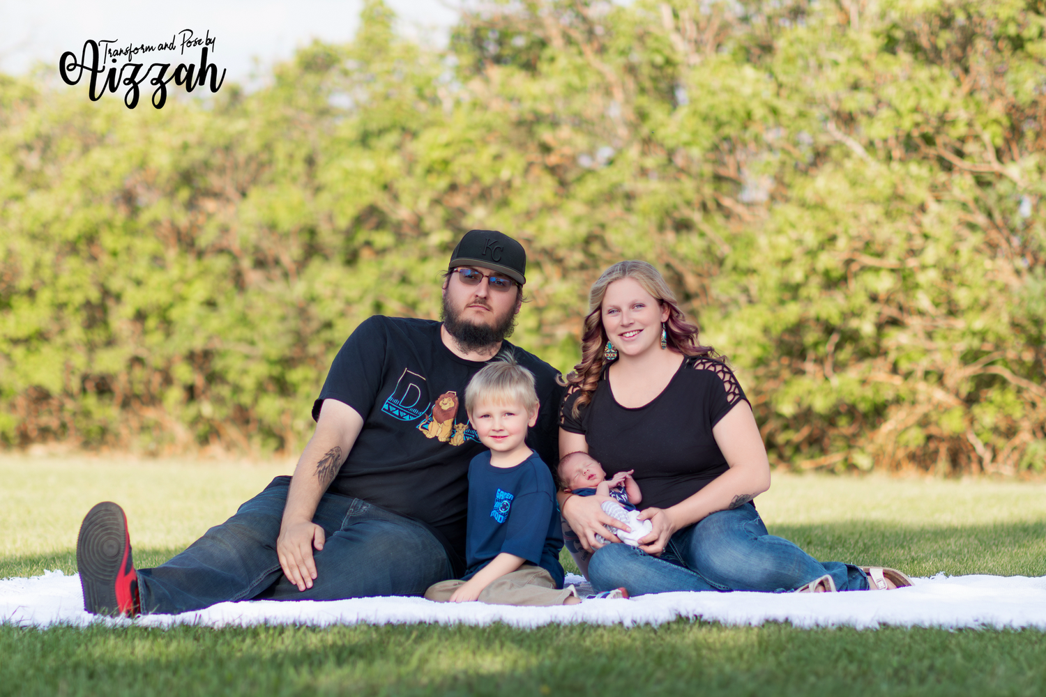 Family sitting together on white blanket outdoors for portrait session.