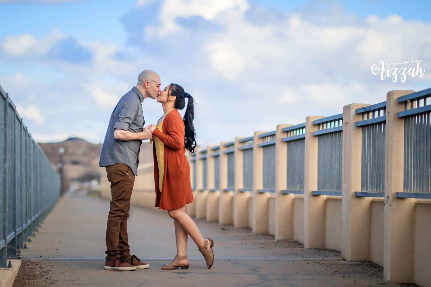 Couple sharing romantic moment on concrete bridge with mountains in background.
