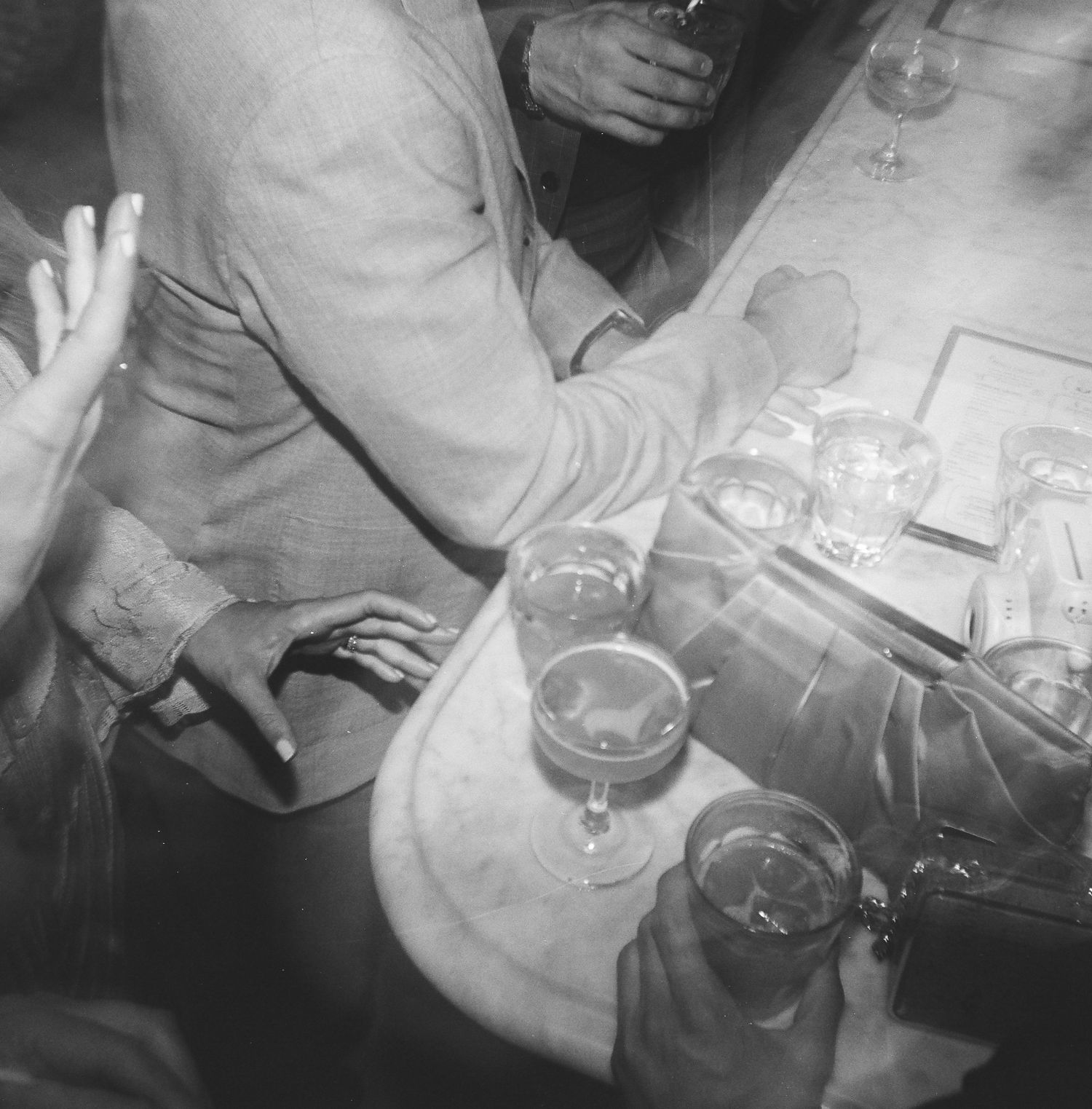 Black and white photo of drinks and hands at a crowded bar counter, captured on 120 film with a Holga 120.