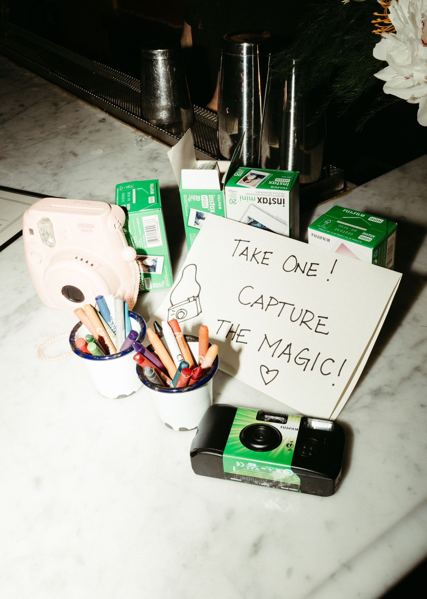Disposable cameras and note saying 'Capture the Magic' displayed on white marble surface.