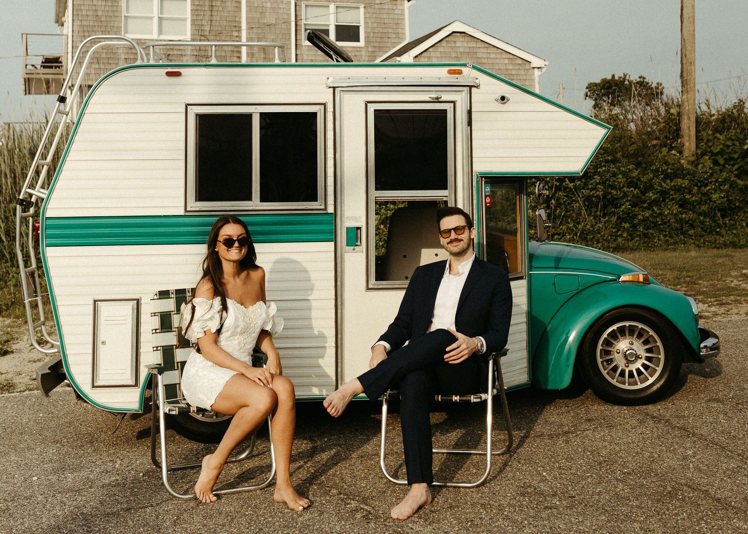 Stylish couple sitting in lawn chairs beside a retro teal Volkswagen camper van.