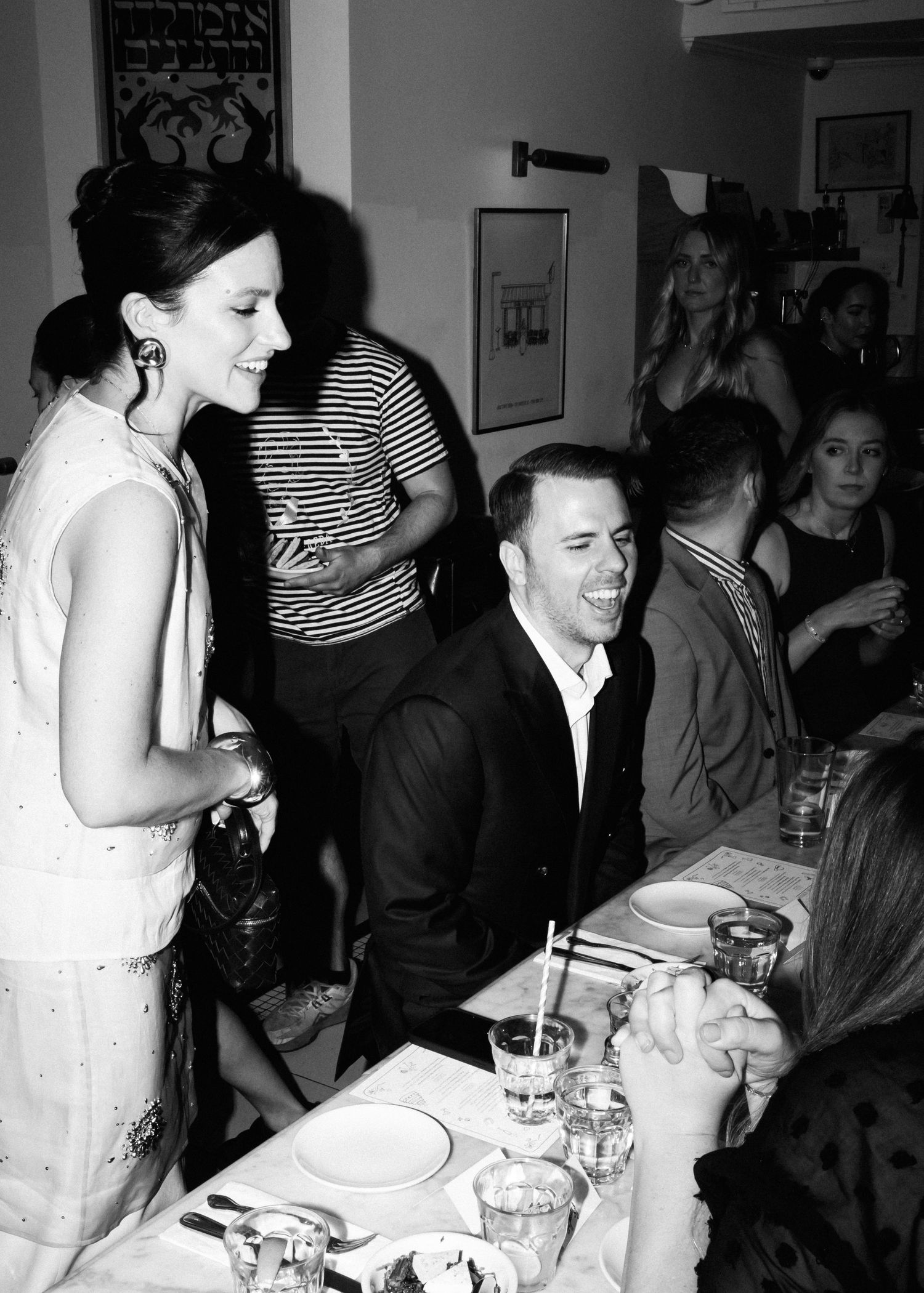 Black and white photo of people dining and socializing at a restaurant table.