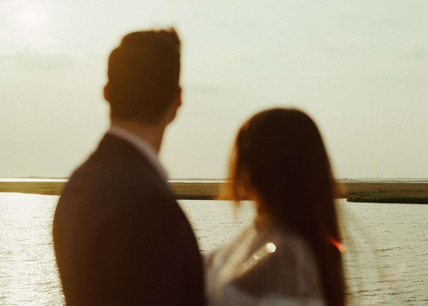Couple sitting together on a wooden dock at sunset overlooking a serene lake.