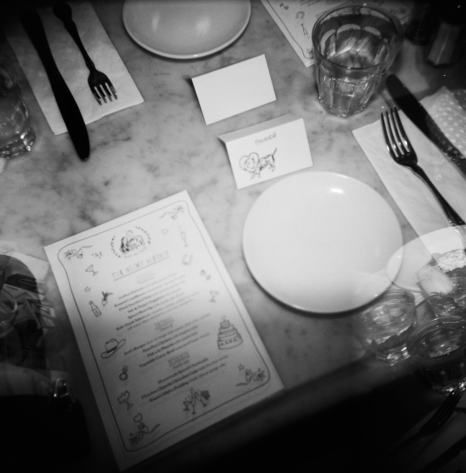 Black and white photo of a restaurant table setting with menu and empty plate, captured on 120 film with a Holga 120.