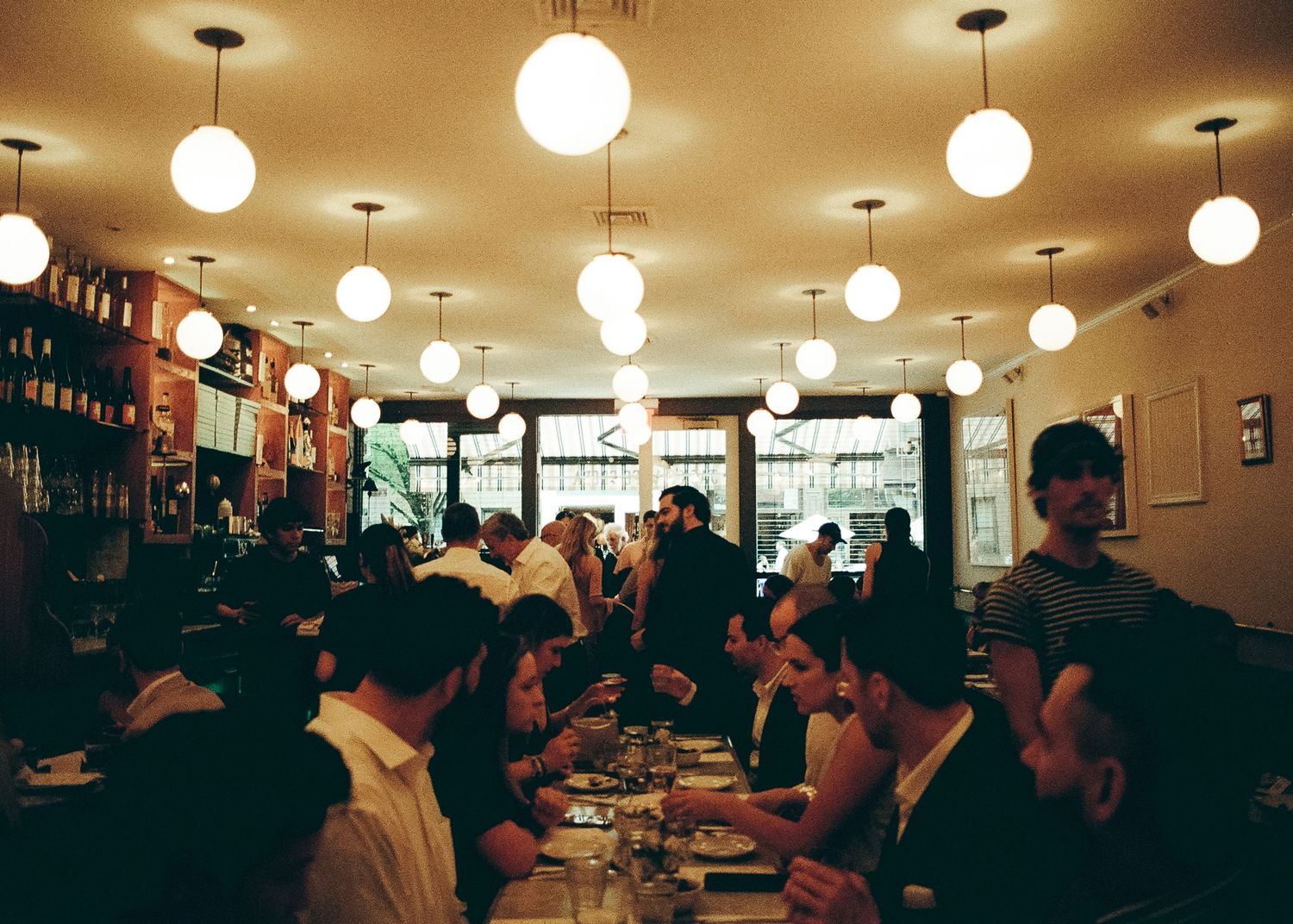 Busy restaurant interior with globe lights and diners seated at tables.