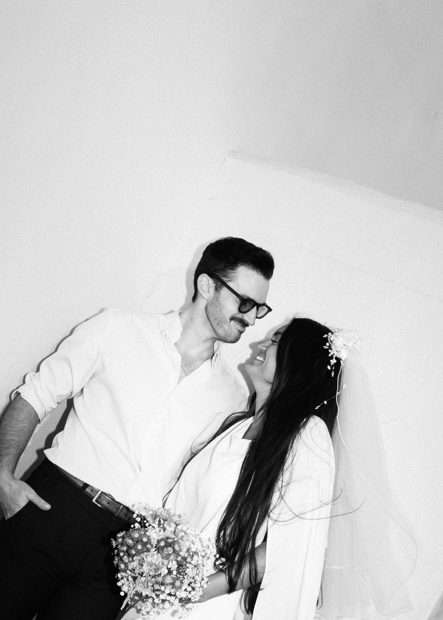 Black and white intimate portrait of couple sharing playful moment with bouquet.