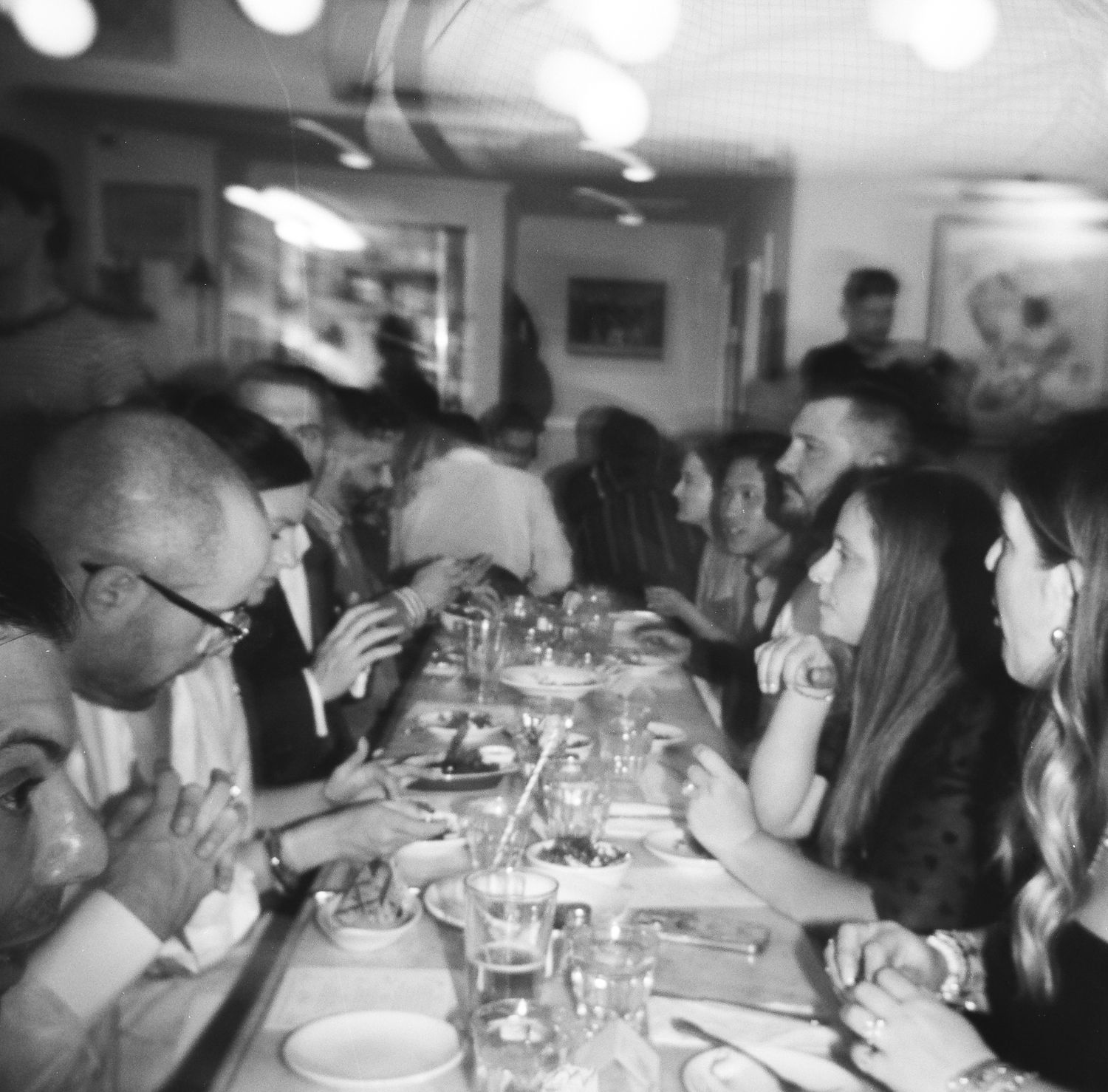 Crowded restaurant table with diners enjoying their meal in black and white, captured on 120 film with a Holga 120.