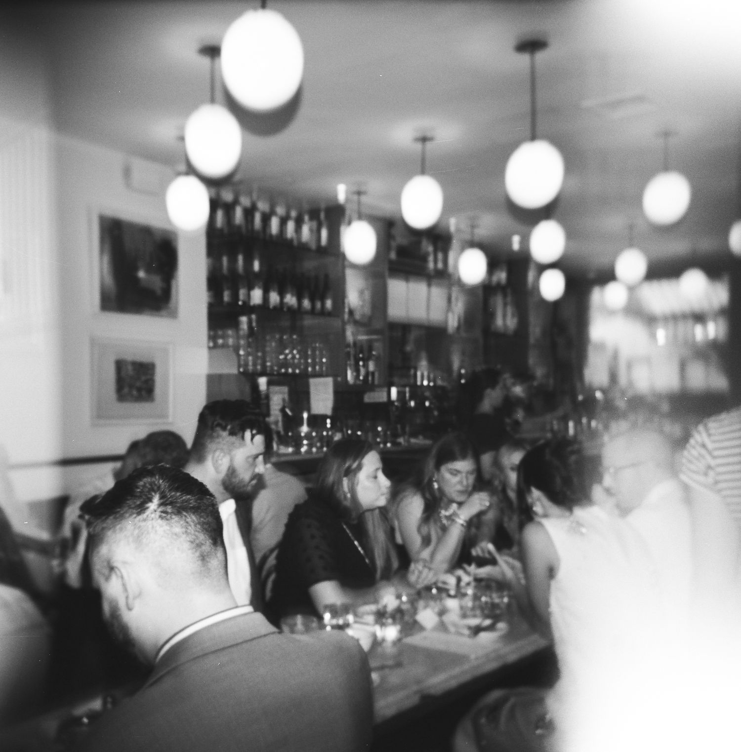 Diners seated at a bar counter under round pendant lights, captured on 120 film with a Holga 120.