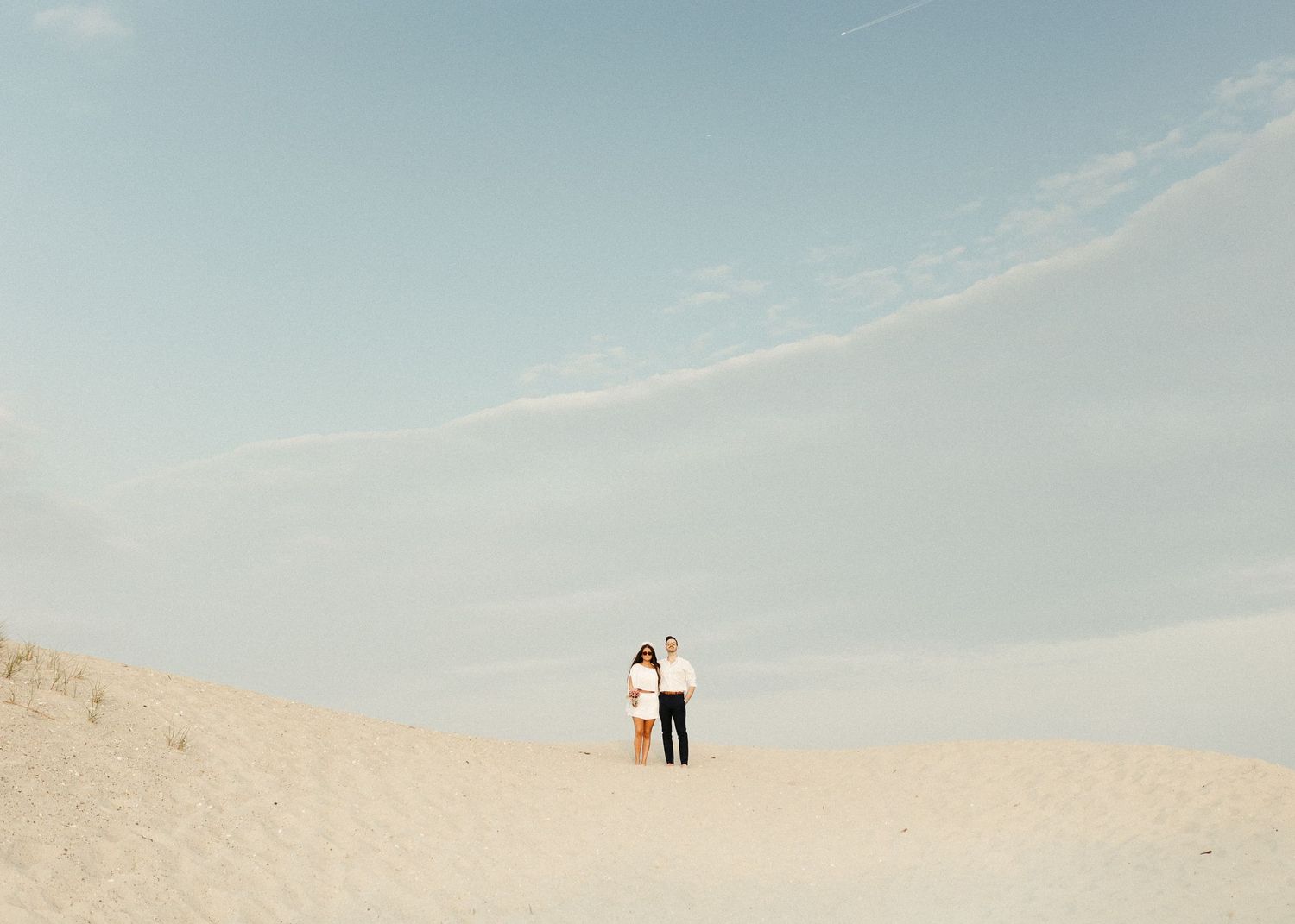 Minimalist desert landscape with distant figures silhouetted against pale blue sky.