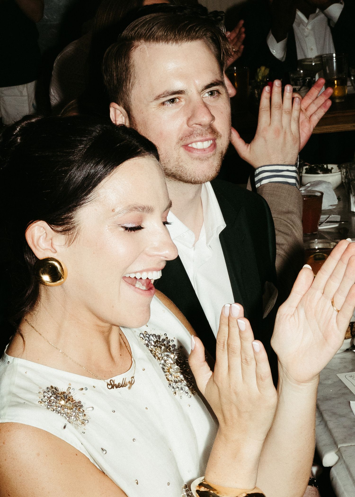 Candid moment at a dinner party with guests laughing and clapping in formal attire.