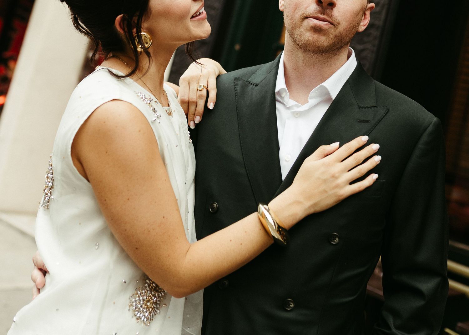 Couple in formal wedding attire sharing intimate moment against brick wall.