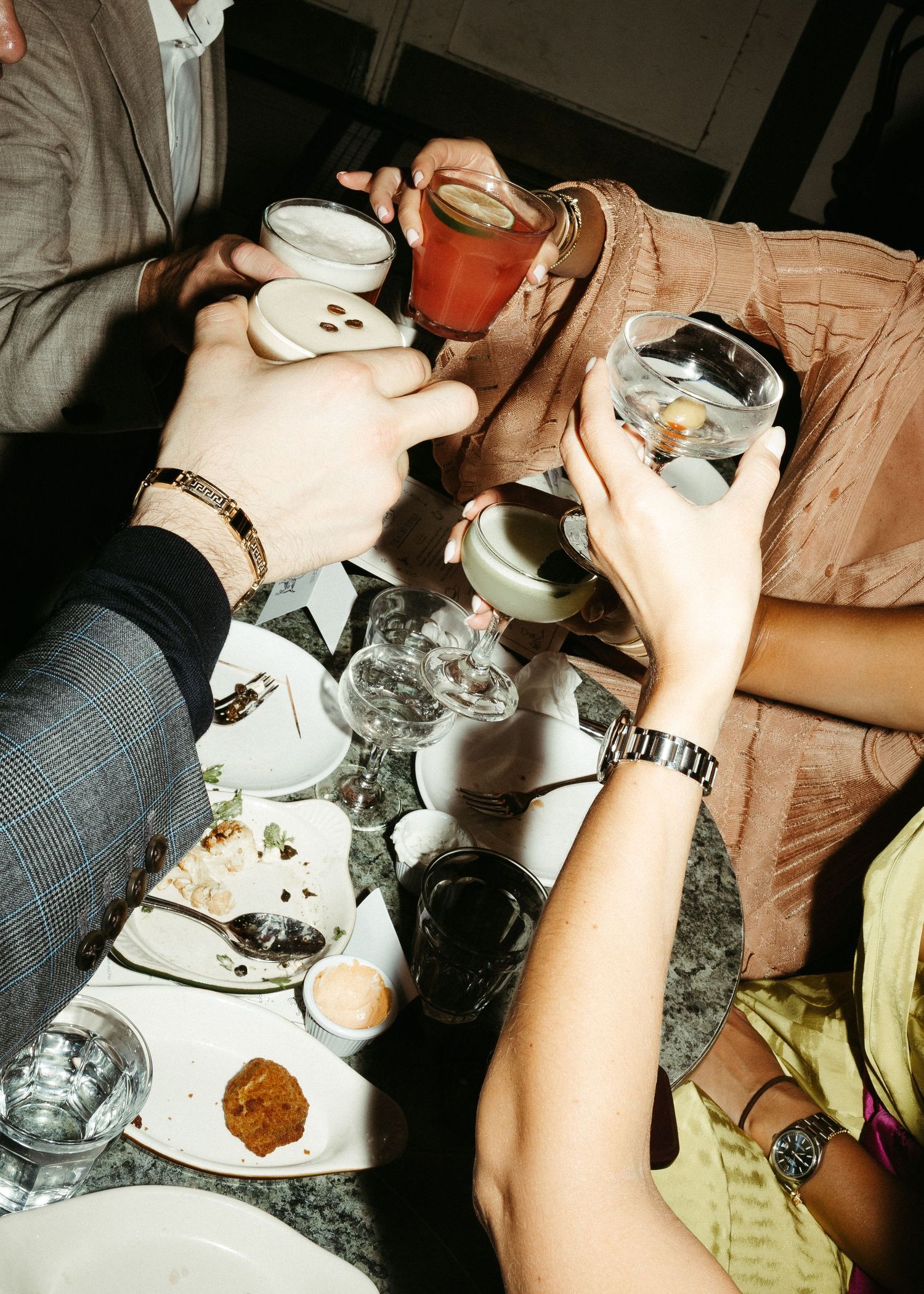 Hands holding drinks and small plates at a social gathering with warm lighting.