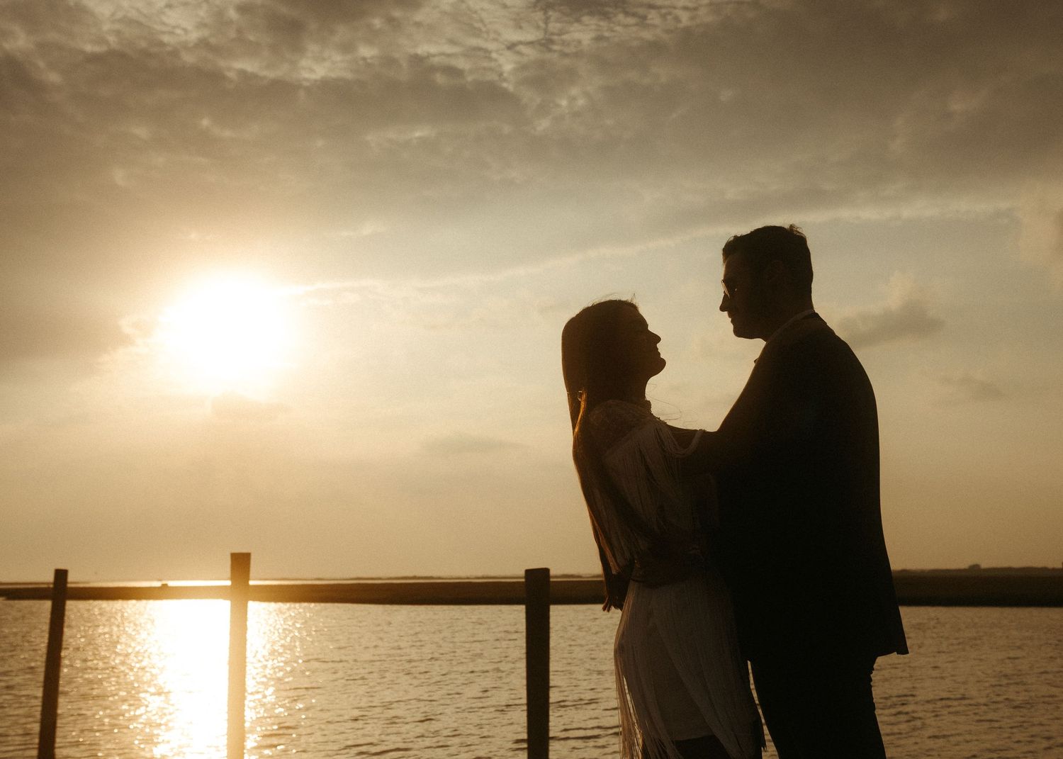 Silhouettes of a couple embrace by the water during a dramatic sunset.
