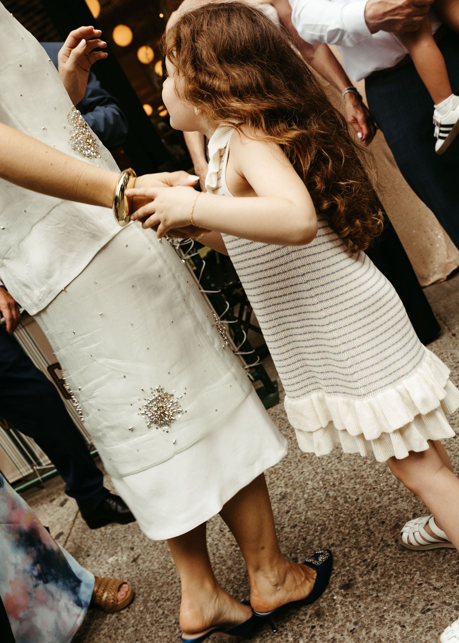 Child in a white ruffled dress interacting with others at an outdoor event.