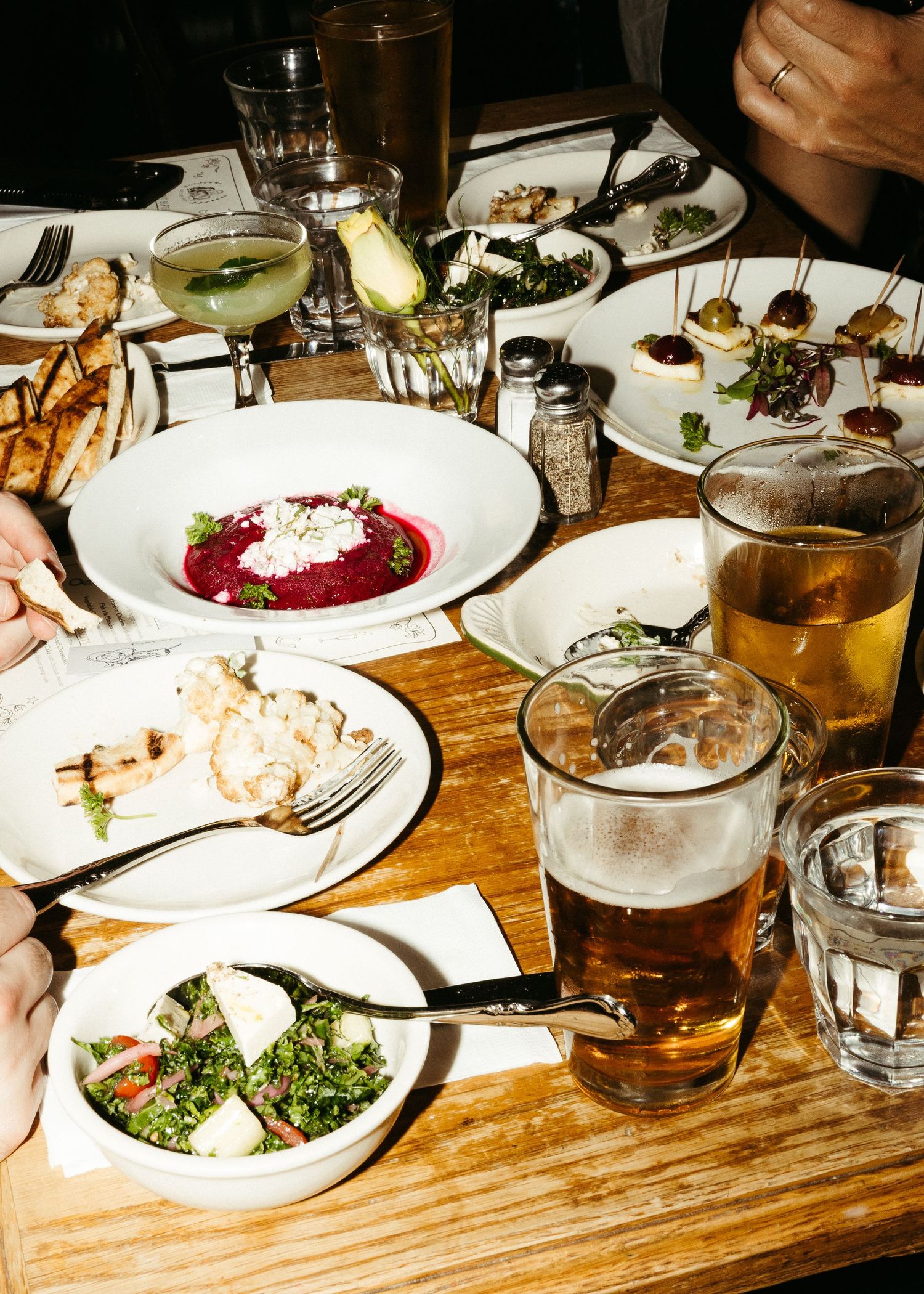 Table spread with various dishes, appetizers, and drinks at a restaurant.