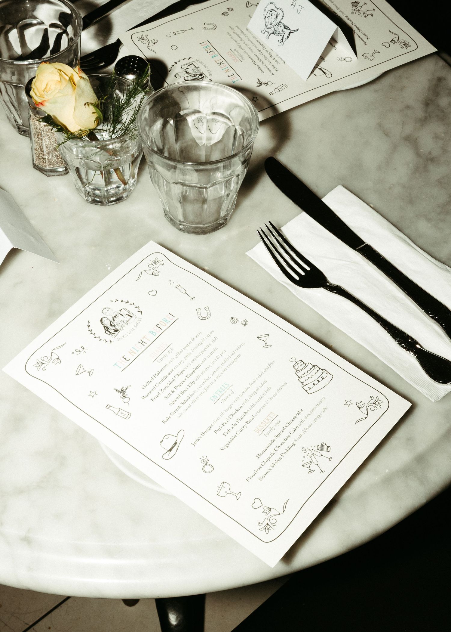 An elegant table setting with decorative menu cards, glassware, and cutlery on a marble surface.