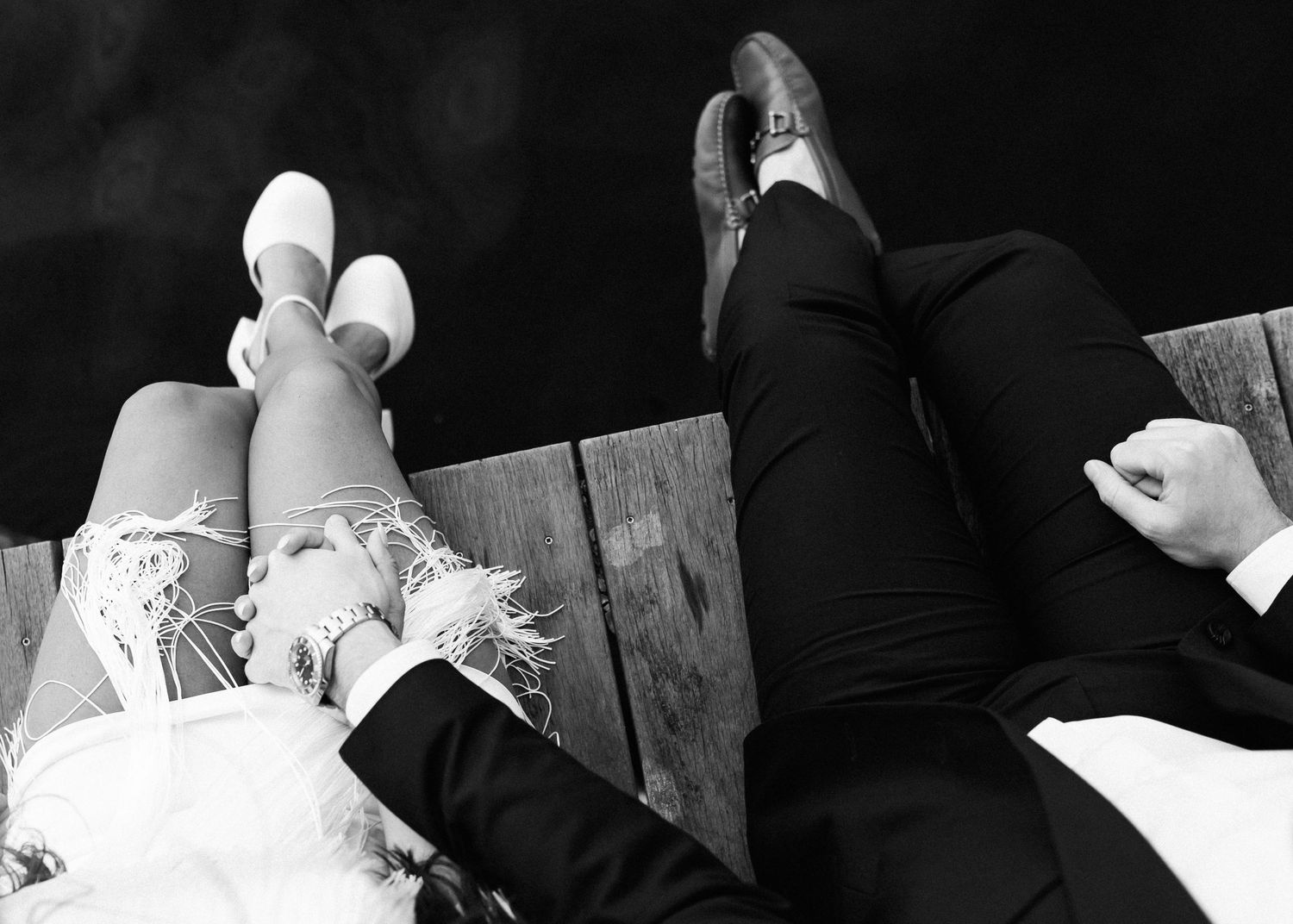 Overhead view of two pairs of feet resting on wooden dock.