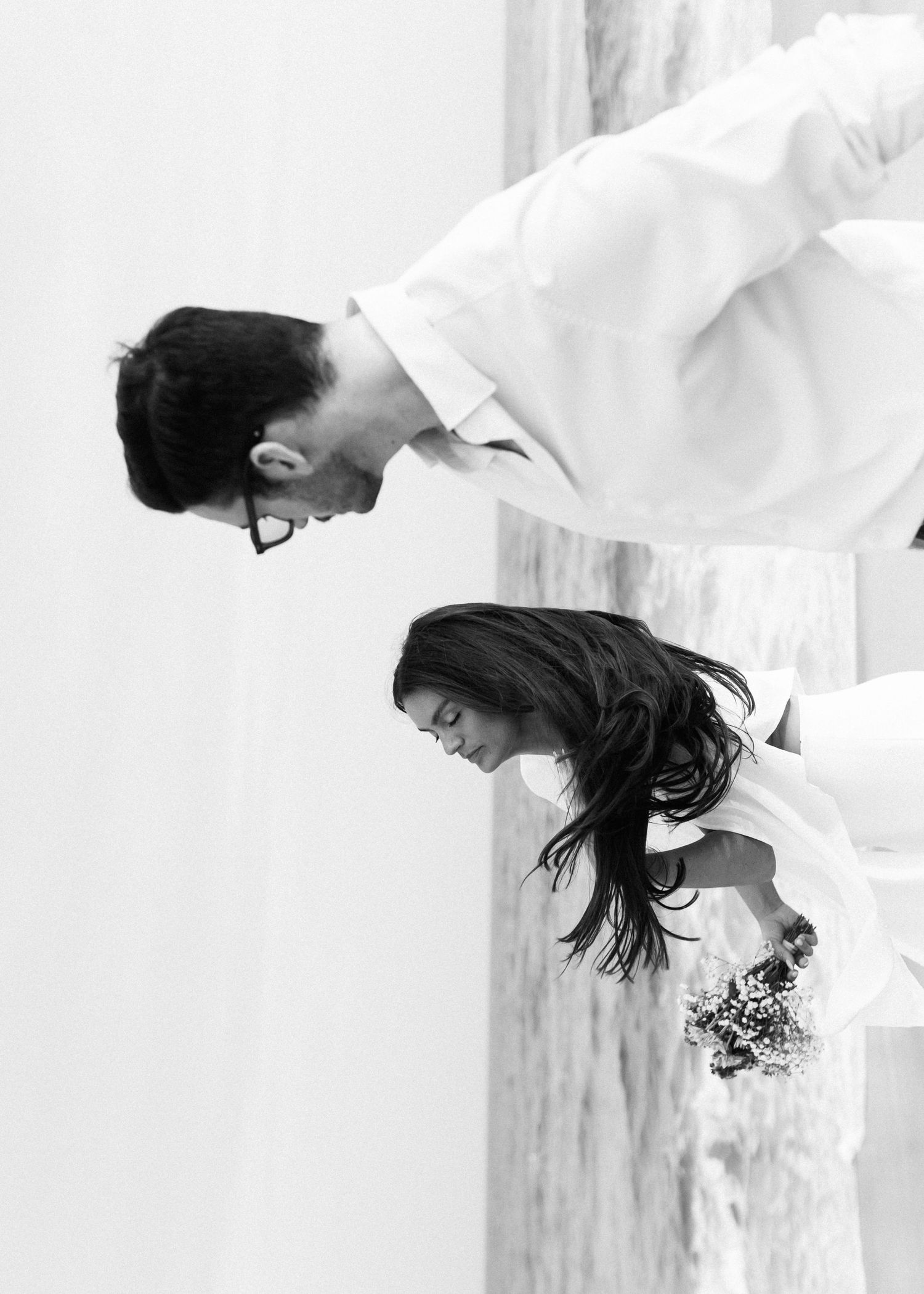 An artistic black and white photo of a couple bending forward on the beach.