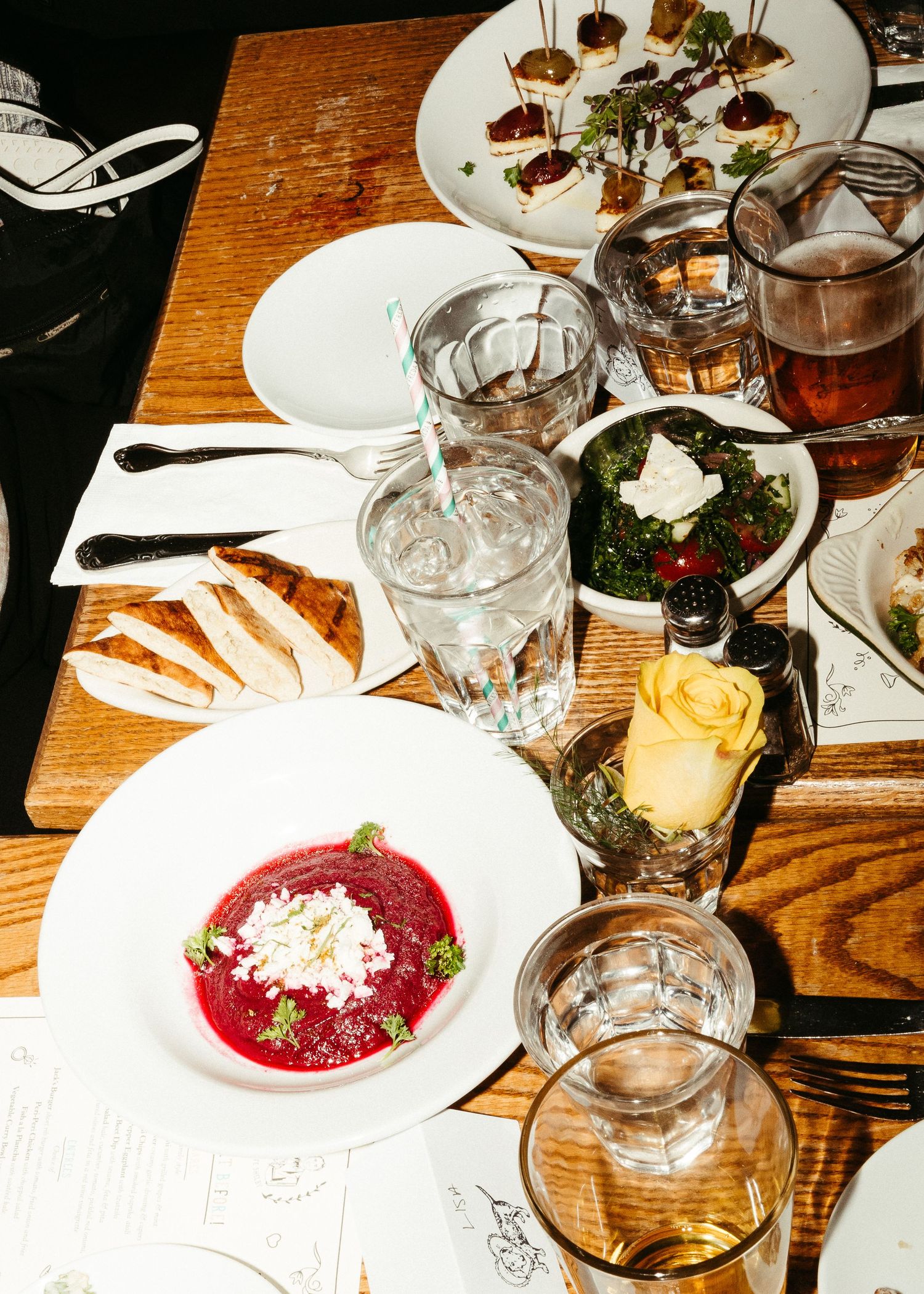 Overhead view of a restaurant table with red soup, cocktails, and shared plates in warm lighting.