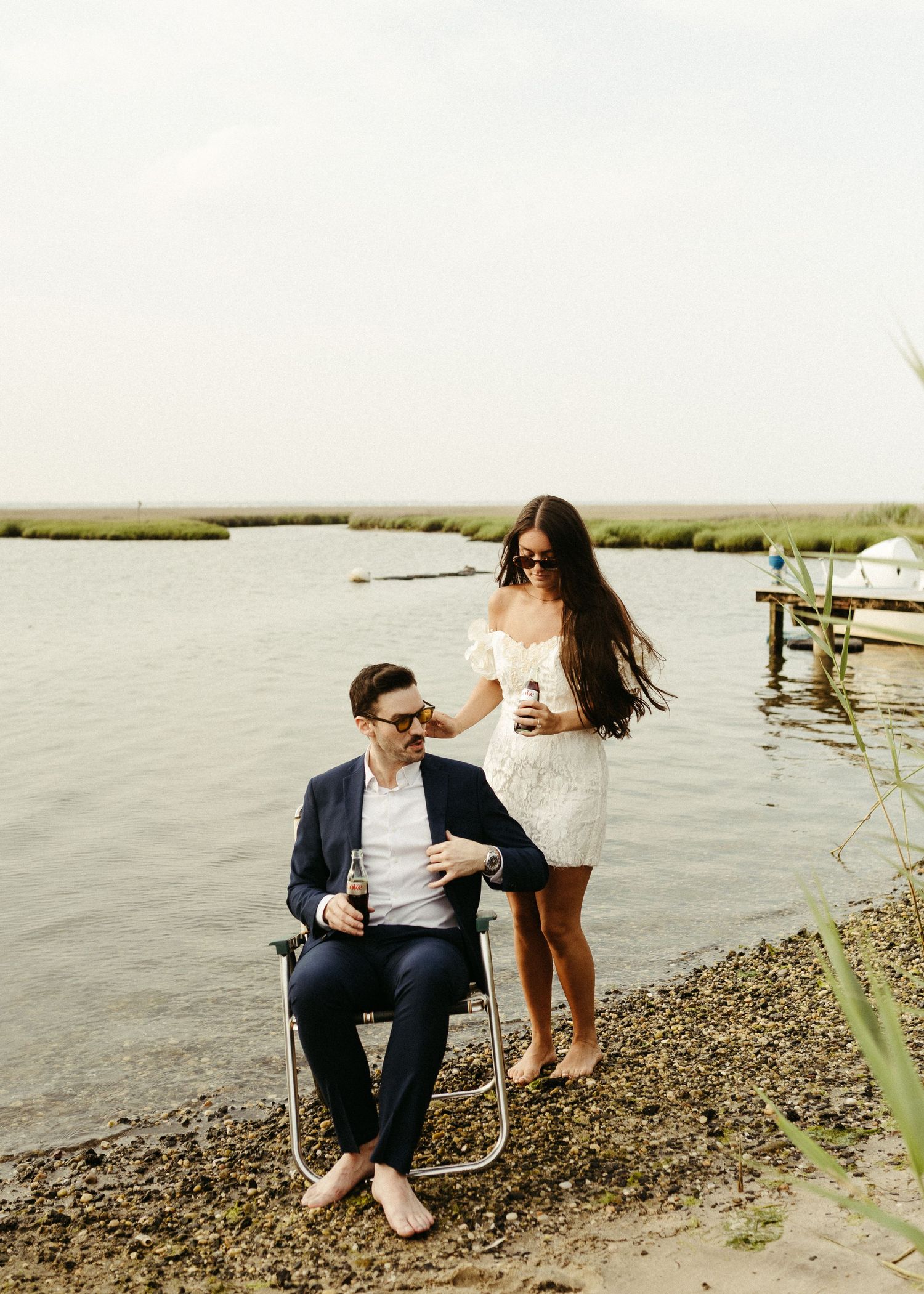 A couple enjoys drinks waterside in vintage-style lawn chairs.