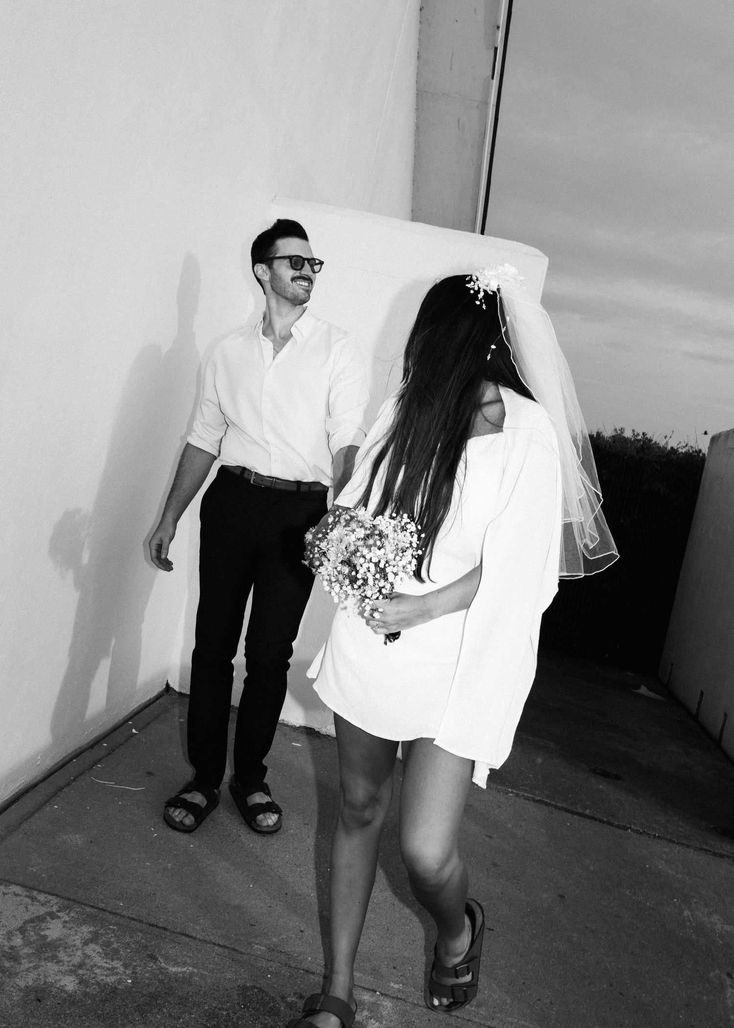 Black and white photo of couple laughing together outdoors, bride holding delicate bouquet.