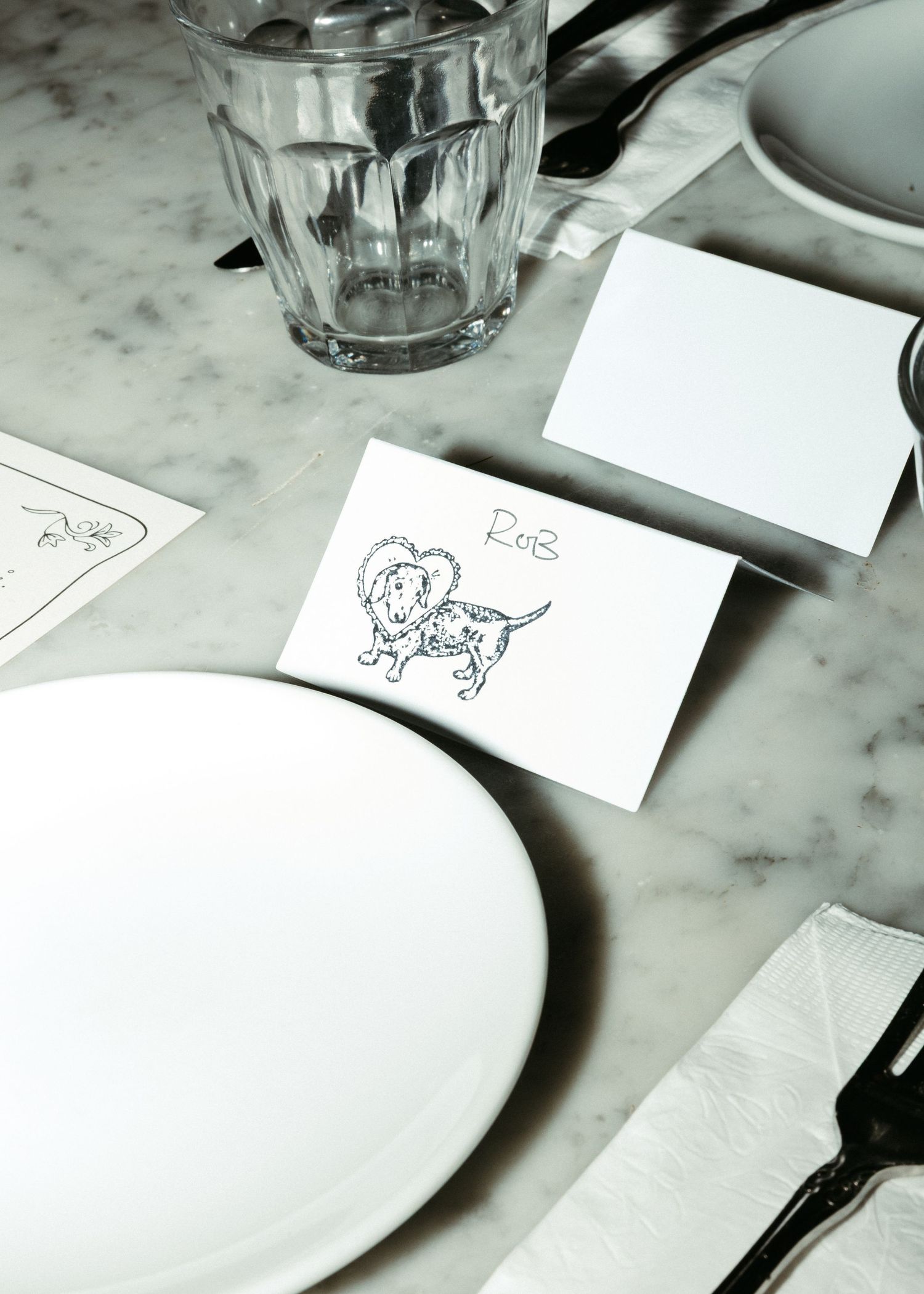 A place setting with white plates and a decorative sketch on a marble table surface.
