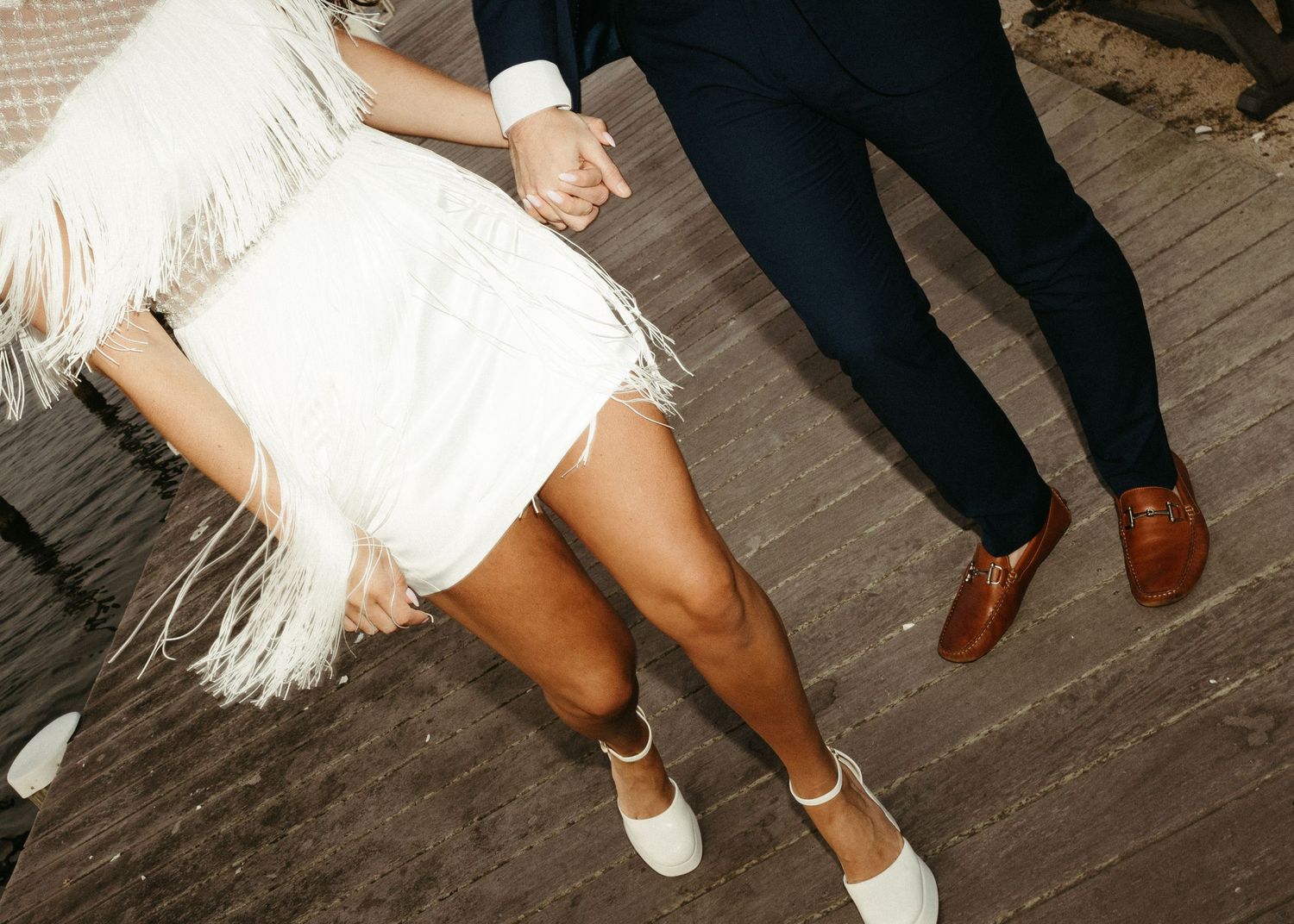 Cropped view of a couple's feet on wooden deck, showing dress shoes and fringe dress details.