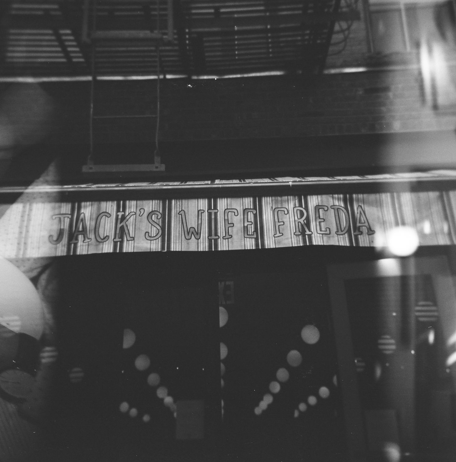 Black and white signage reading 'Jack's Wife Freda' with pendant lights below, captured on 120 film with a Holga 120.