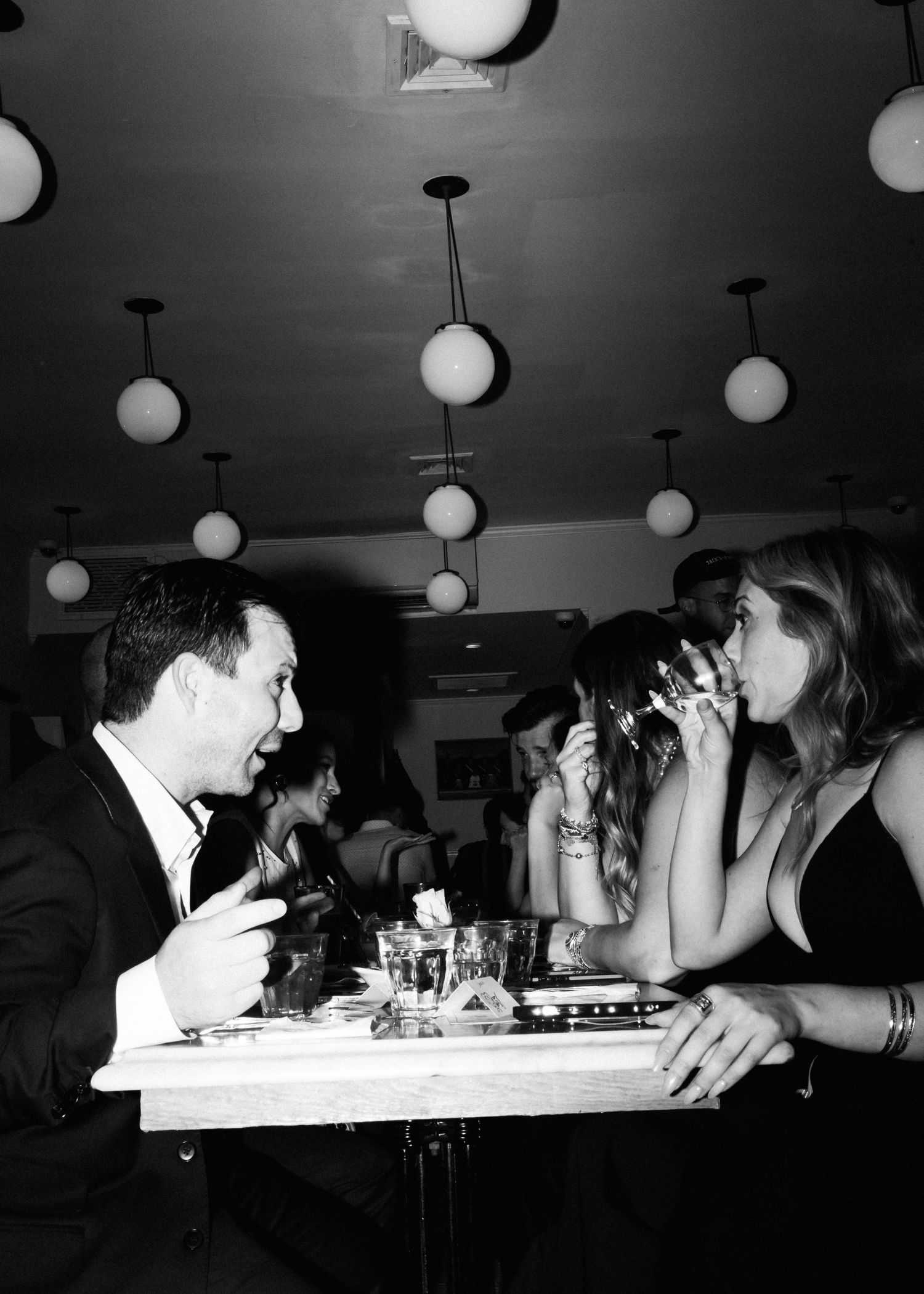 Black and white photo of diners enjoying a meal under spherical pendant lights.