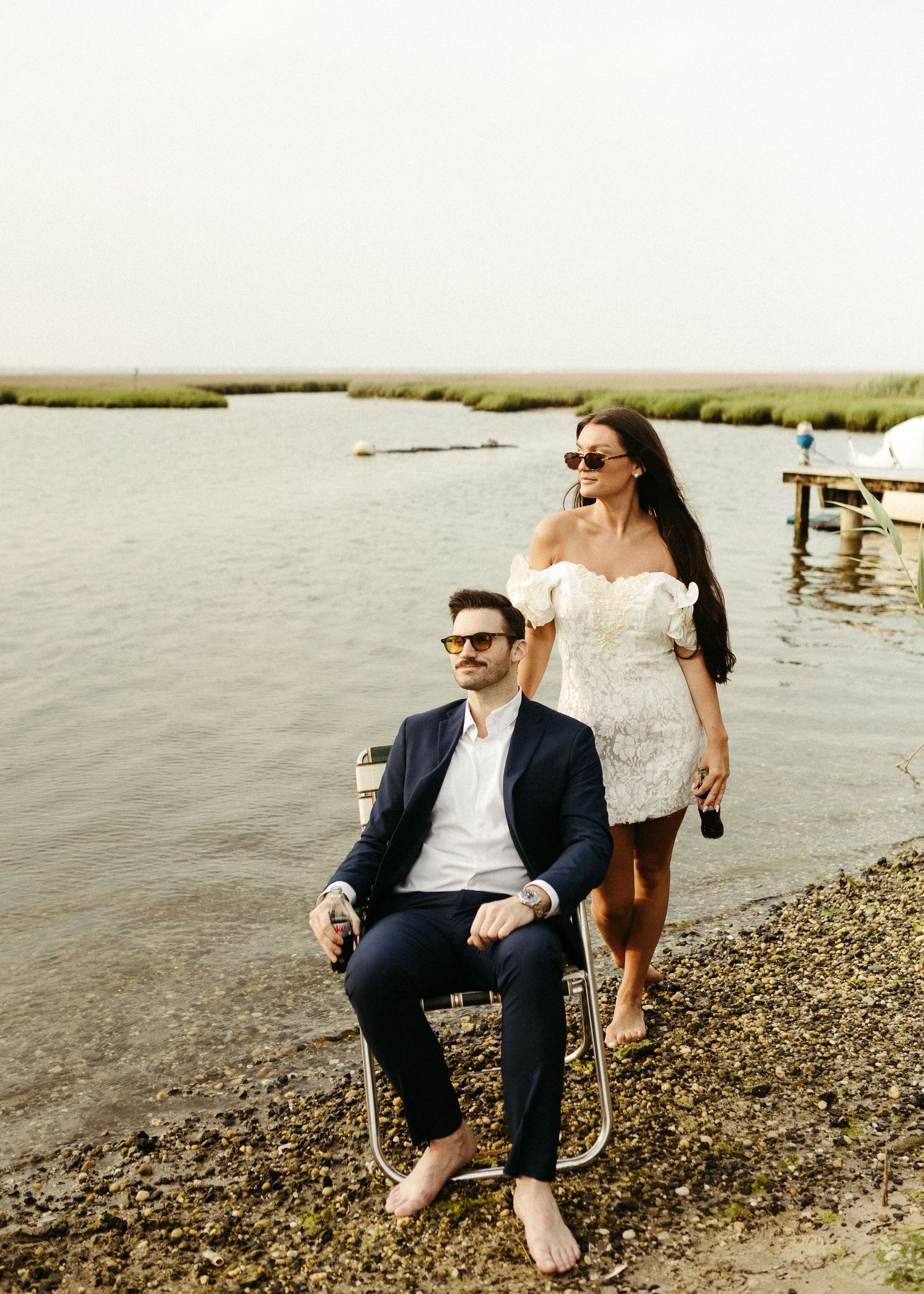 A couple enjoys drinks by the water's edge in casual summer attire.
