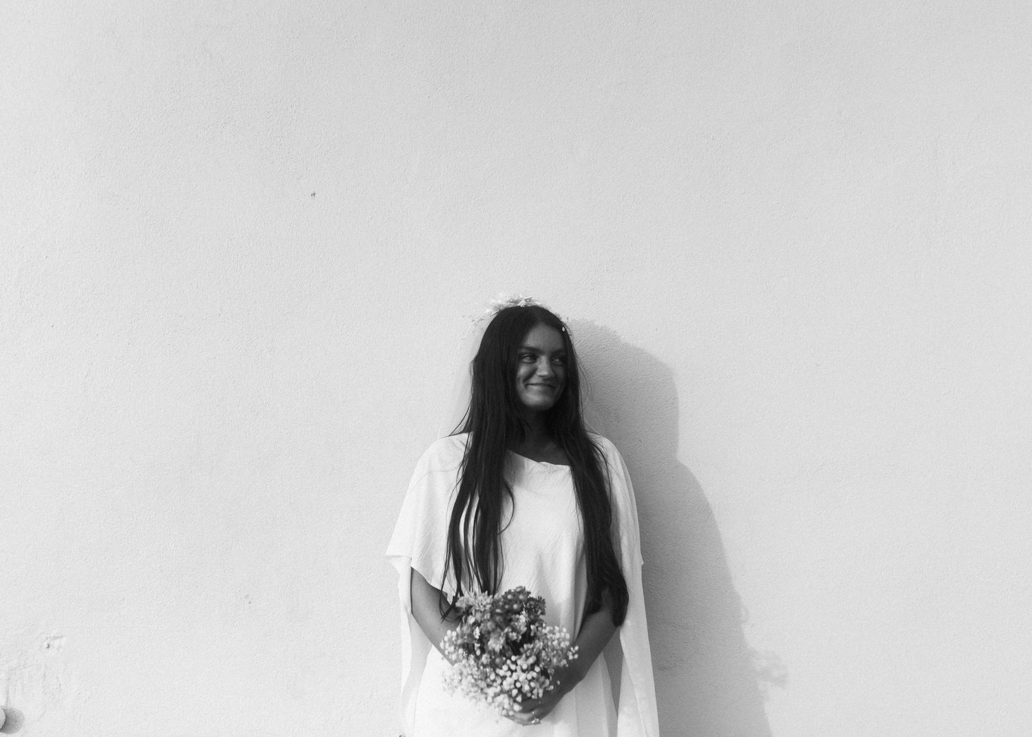 A bride with long dark hair holds a bouquet in a minimalist black and white portrait.