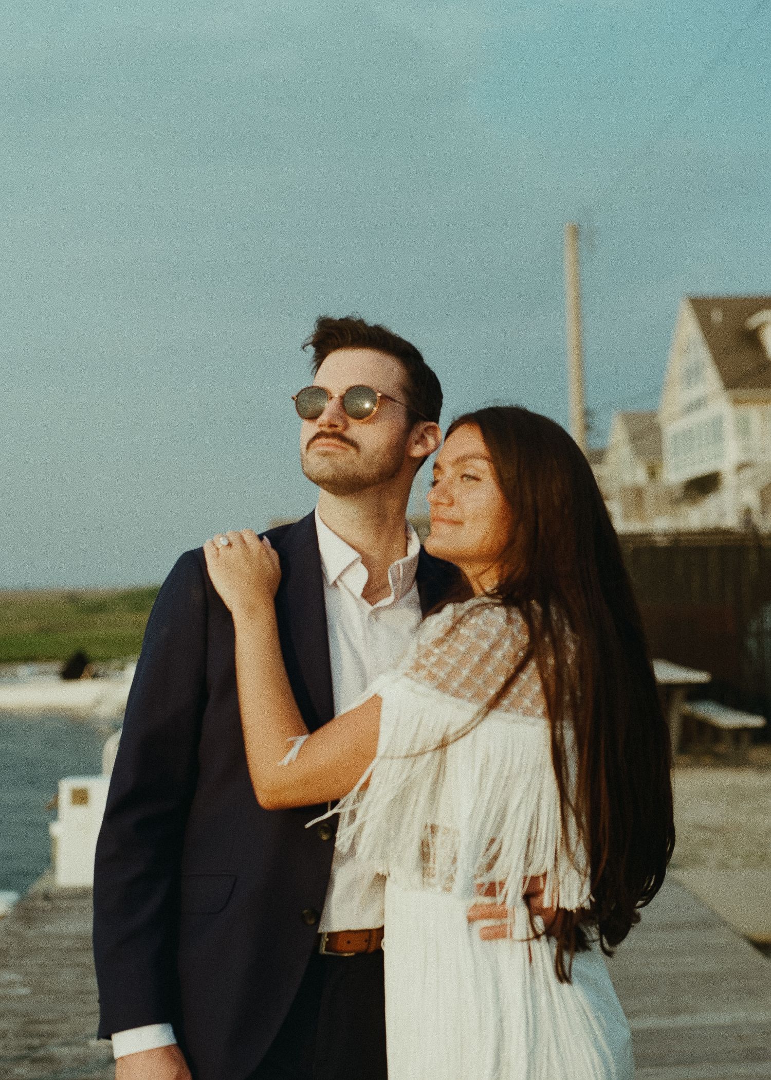 Sunset coastal portrait of couple in formal wear embracing on seaside boardwalk.