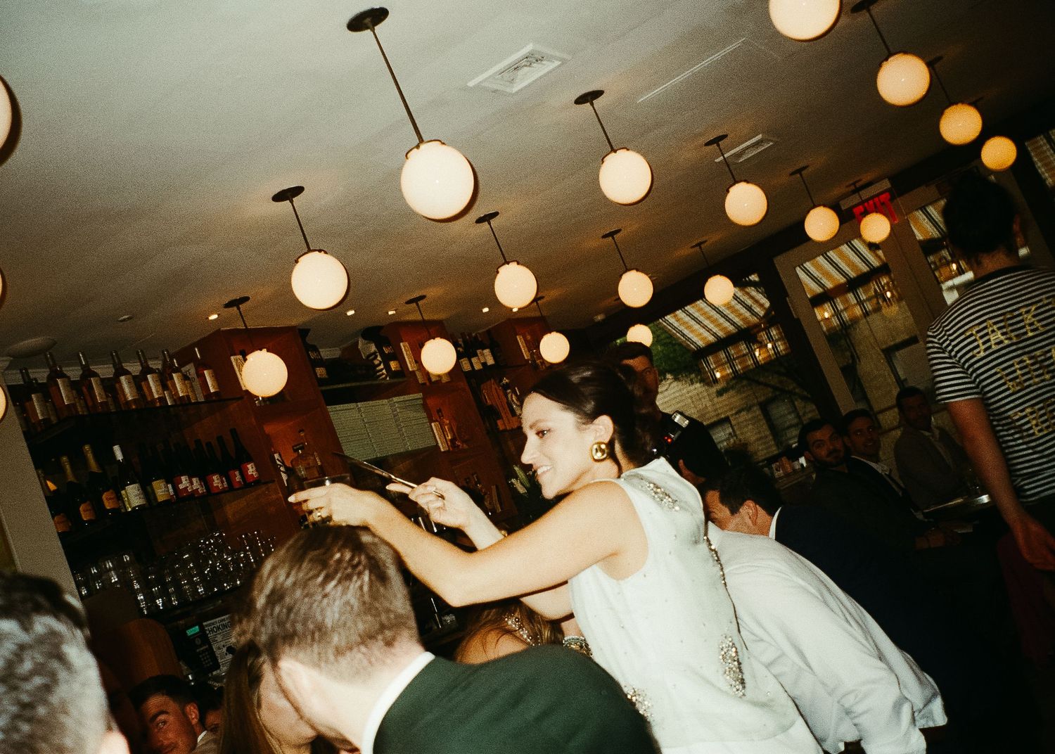 Rehearsal dinner celebration with dancing under pendant lights in restaurant setting.