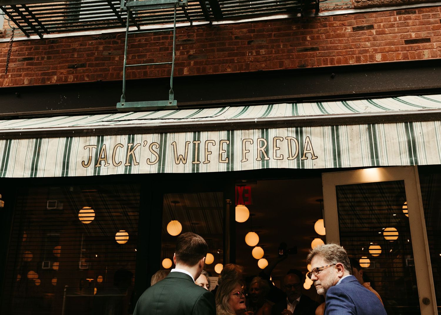 Exterior view of Jack's Wife Freda restaurant with hanging lights and brick wall.