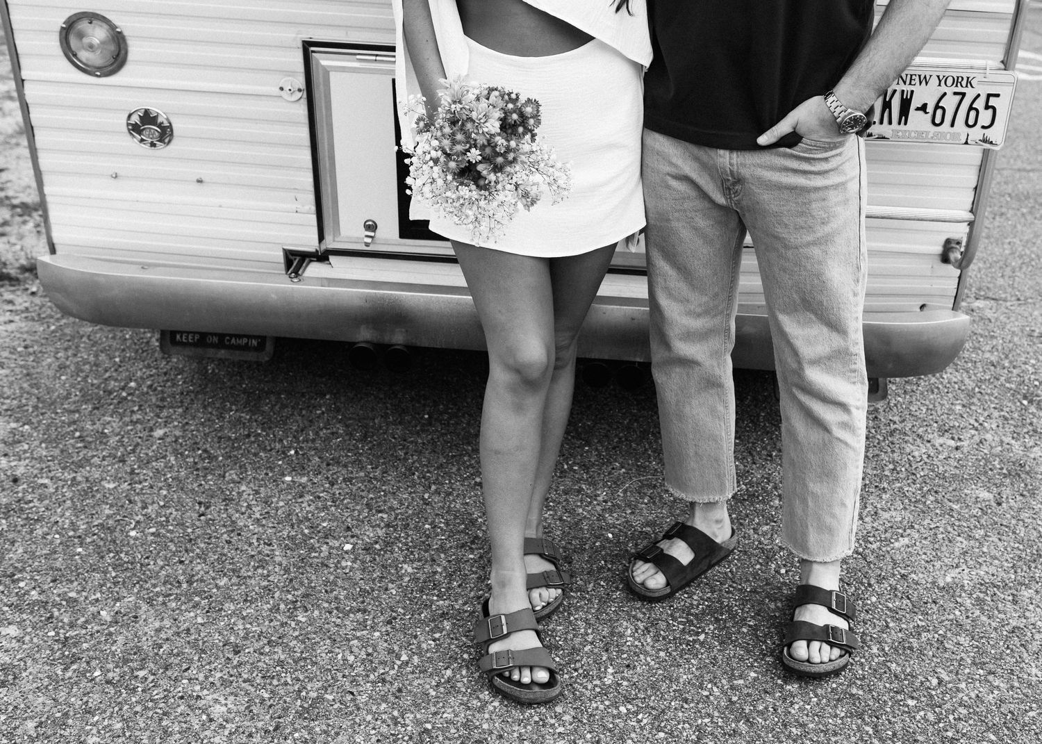 Black and white photo showing feet and legs near a vintage camper.