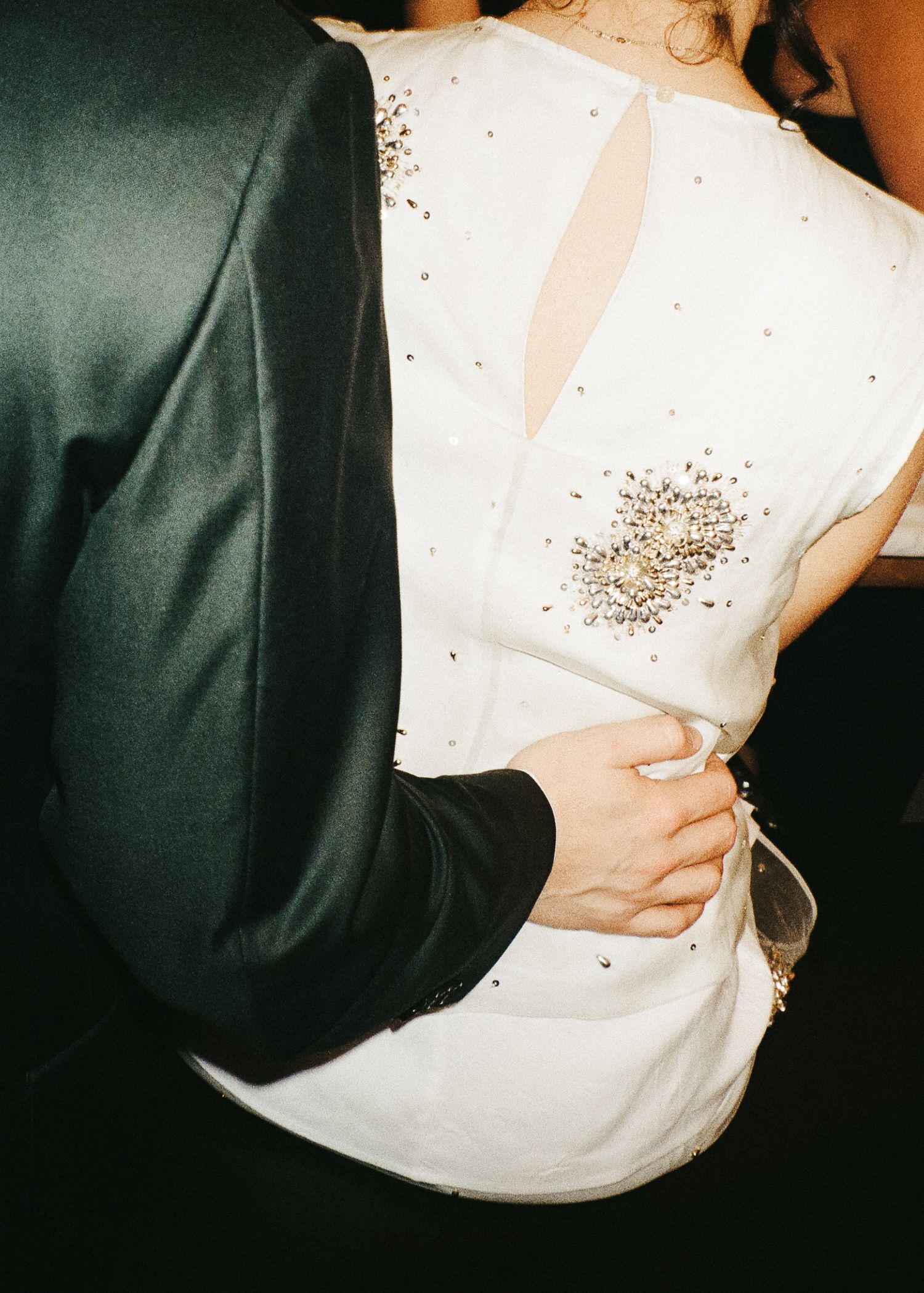 Close-up of formal attire showing dark suit jacket and white beaded dress detail.