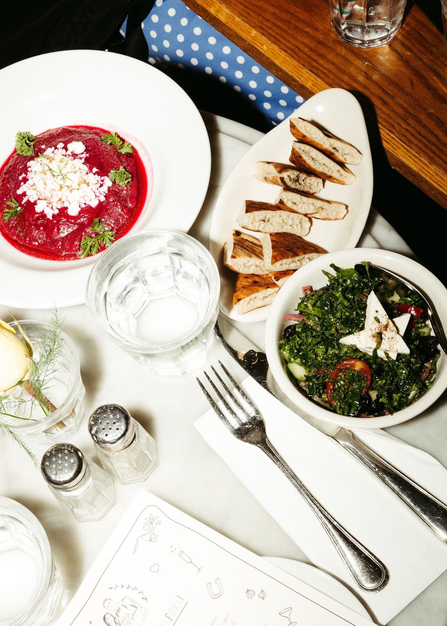 Elegant table setting with beet soup, sliced bread, and fresh green salad on white plates at a restaurant.