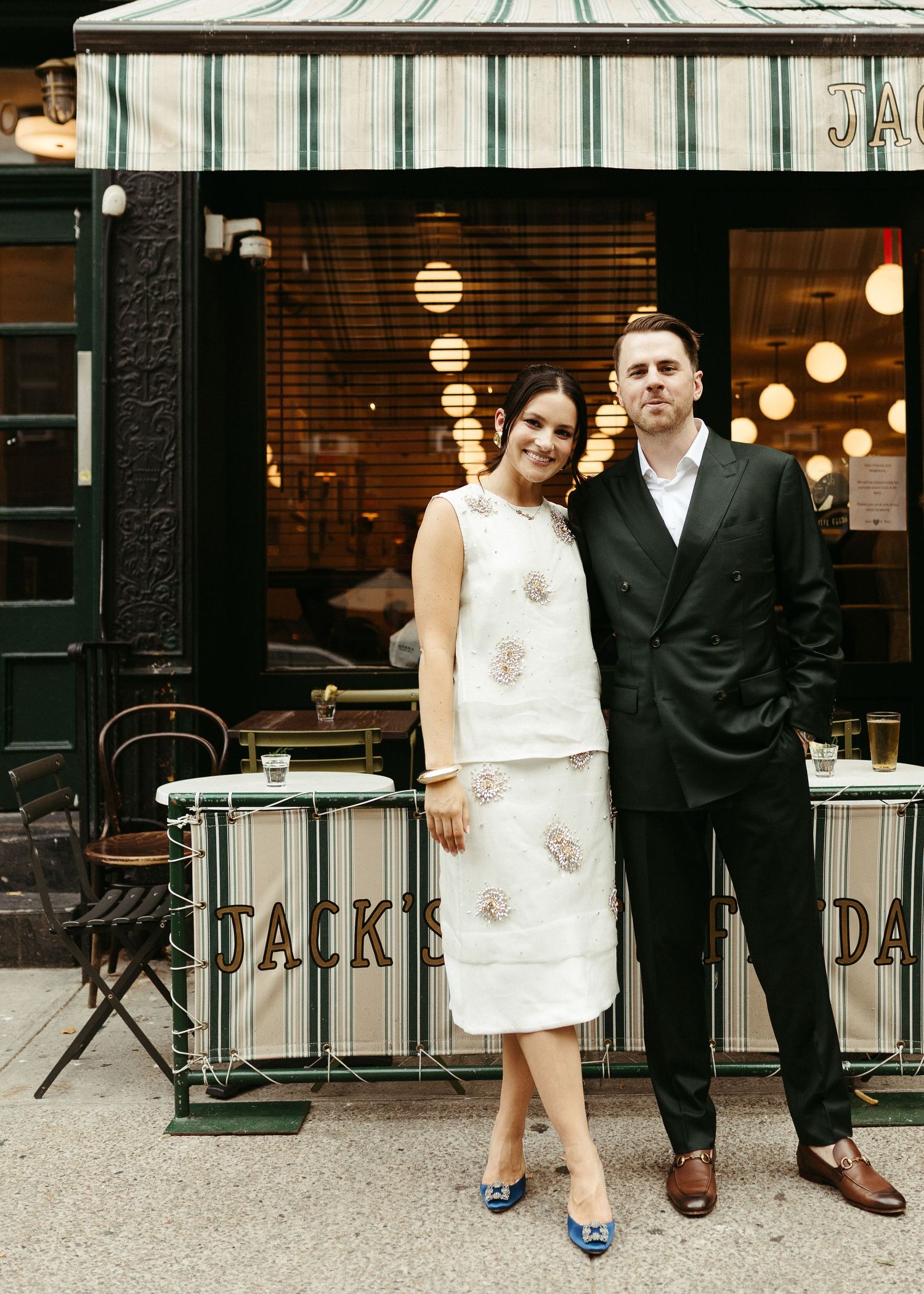 Couple in formal attire standing outside Jack's Wife Freda restaurant, West Village NYC, with vintage storefront and lights.