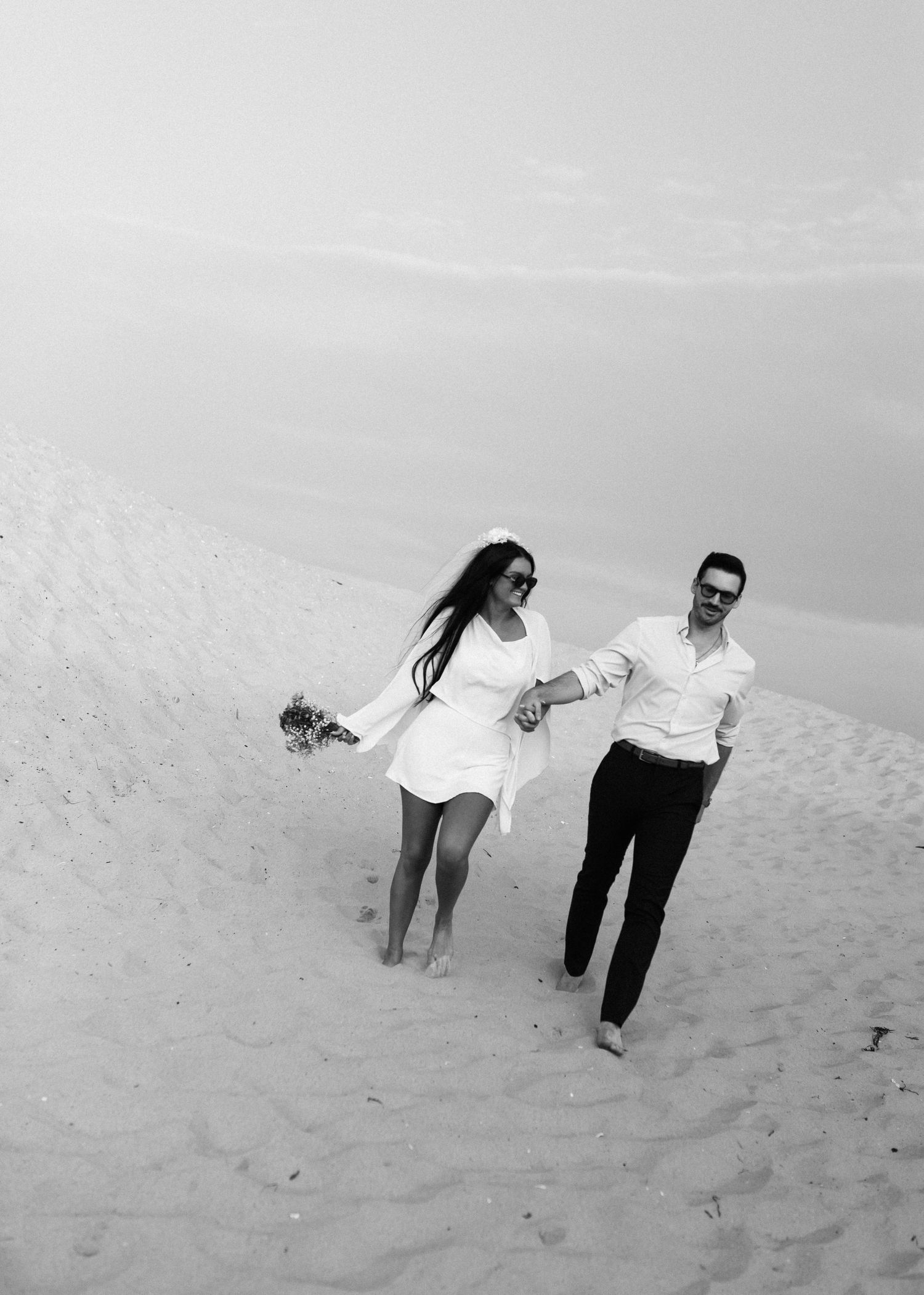 Black and white photo of people playing and running down sandy dunes.