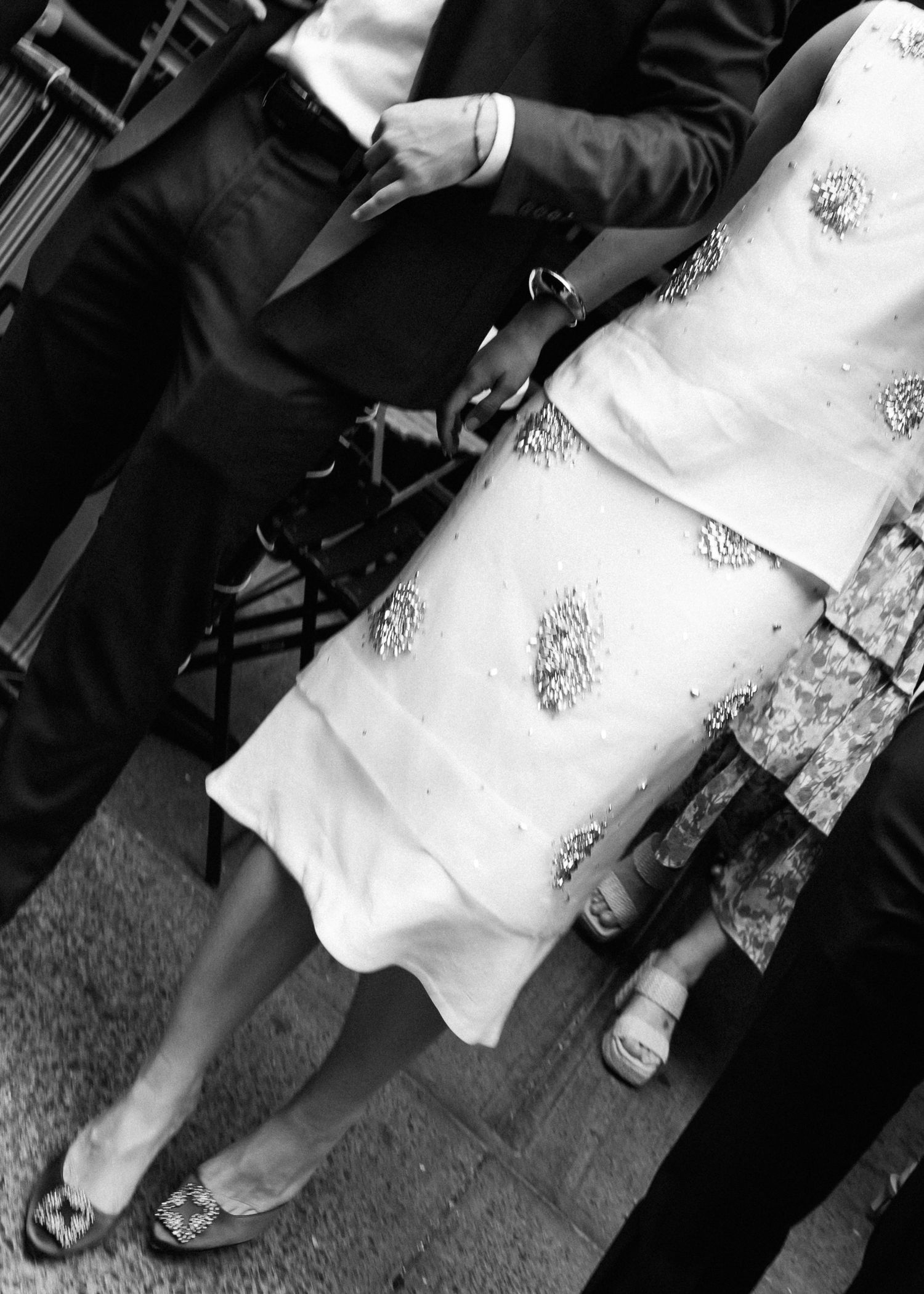 Close-up of formal attire with white embellished dress fabric and black suit.