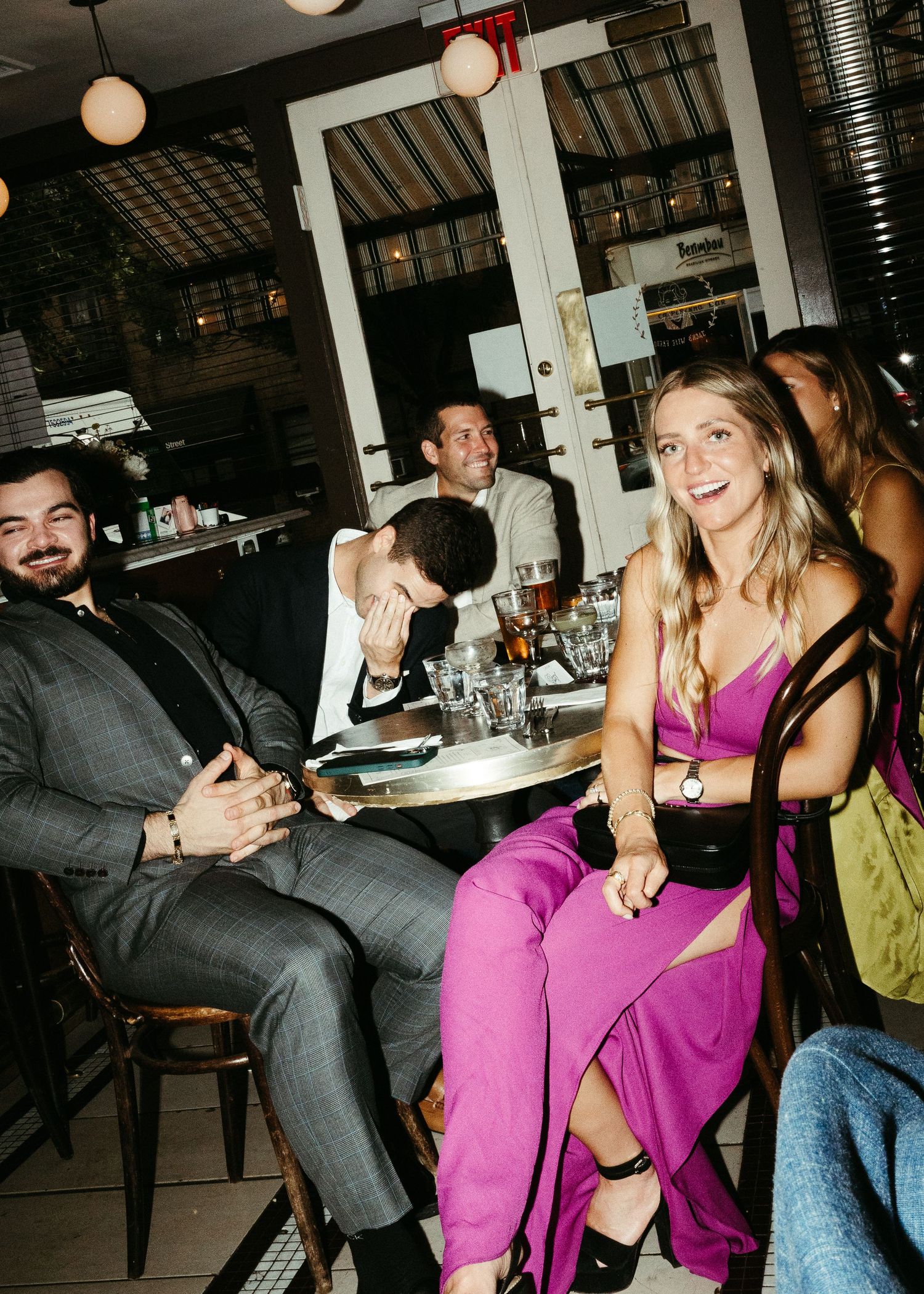 Dinner party guests in formal attire sharing laughter at a restaurant table.
