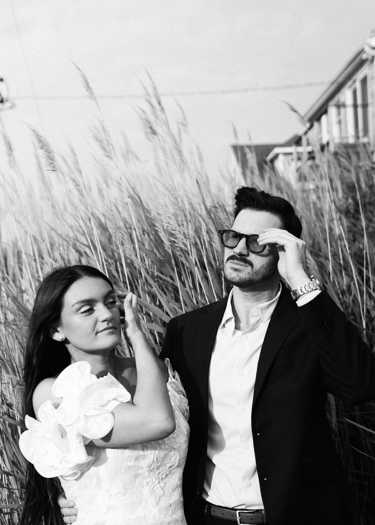 A romantic black and white portrait amid swaying beach grass at golden hour.