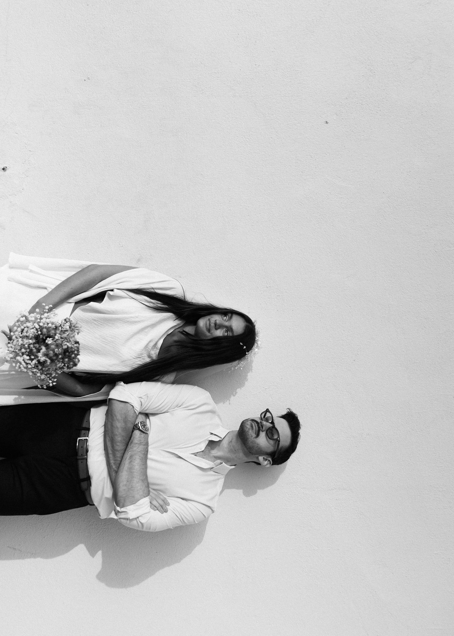 Two people walk up a snowy hill in white formal attire creating dramatic silhouettes.