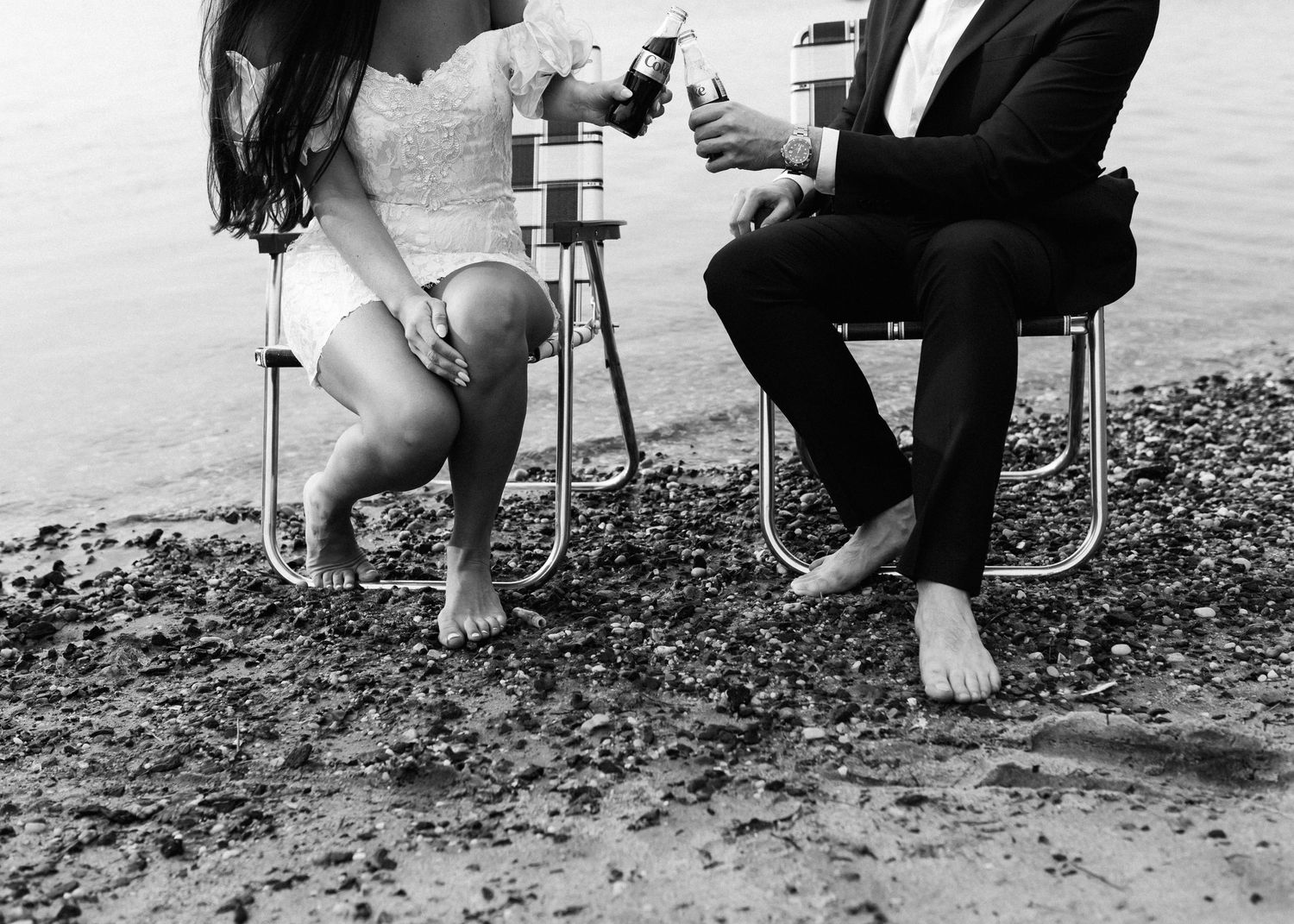 Black and white photo of two people sitting in beach chairs by the water.