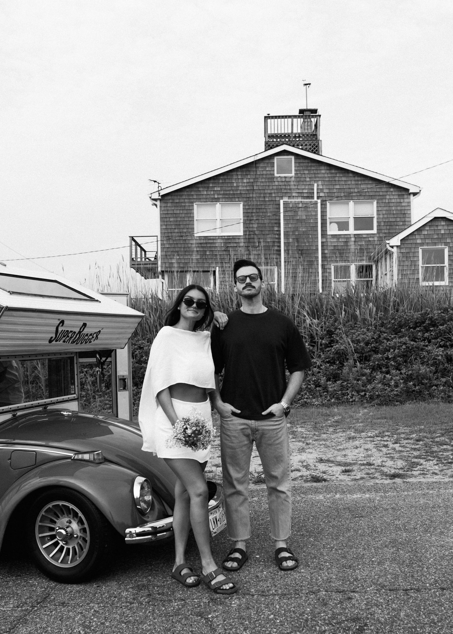 Black and white portrait with vintage VW Beetle and beach house in background.