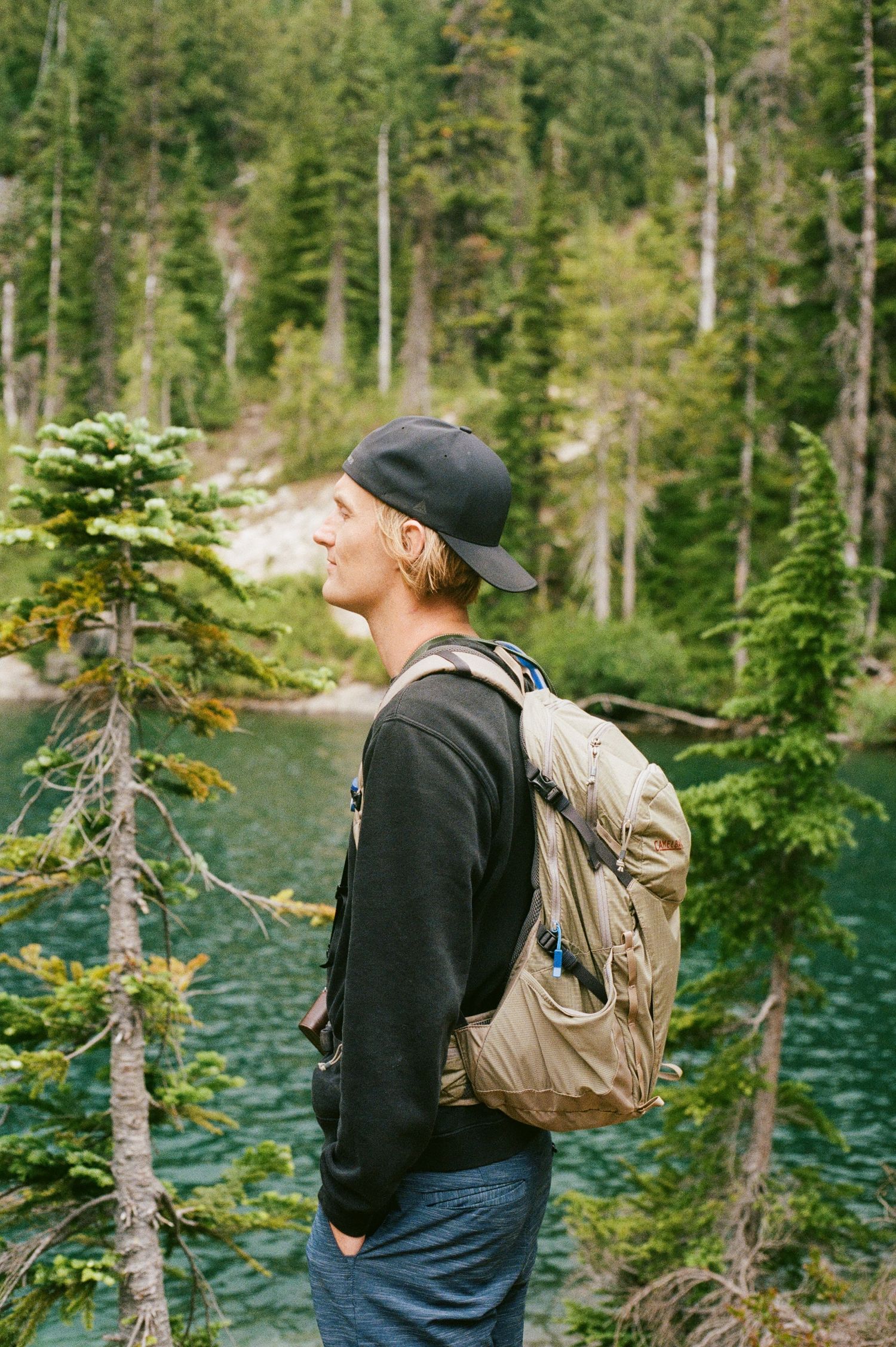 Person with backpack explores scenic mountain lake surrounded by evergreen forest on sunny summer day.