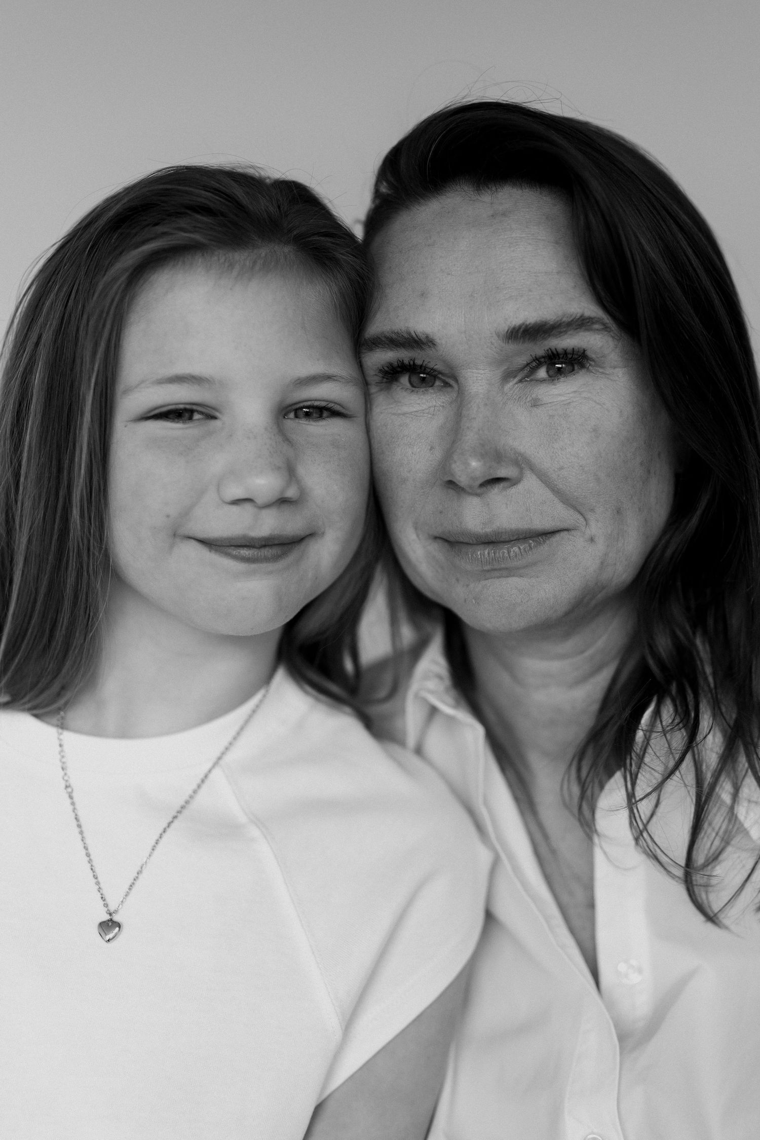 Black and white portrait of a woman and young girl in white shirts smiling together, likely mother and daughter.