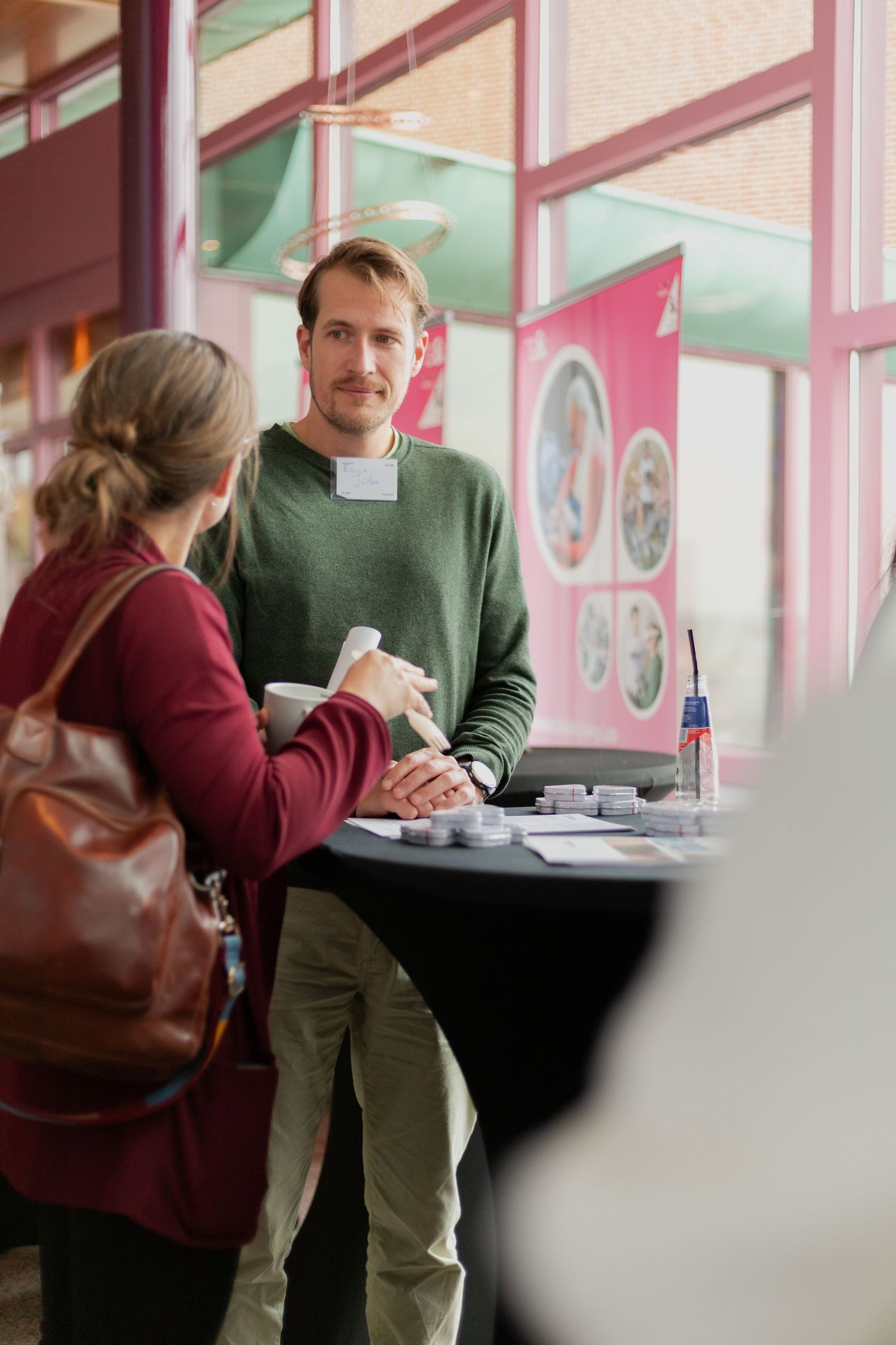 Two people sit at a table having a conversation in a bright pink and green interior space.