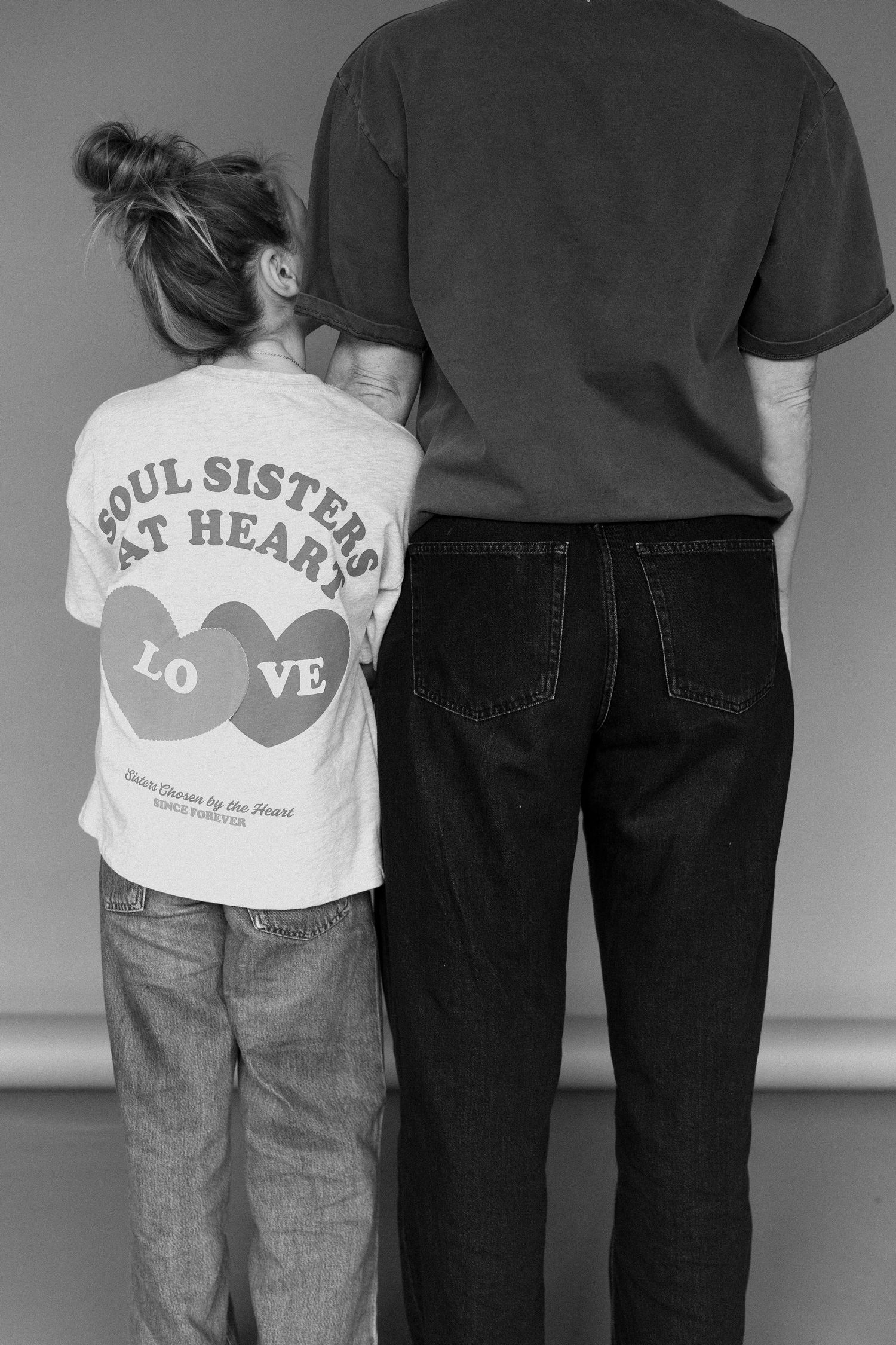 Black and white photo of a child in a Soul Sisters at Heart tee standing beside an adult, both facing away from camera.