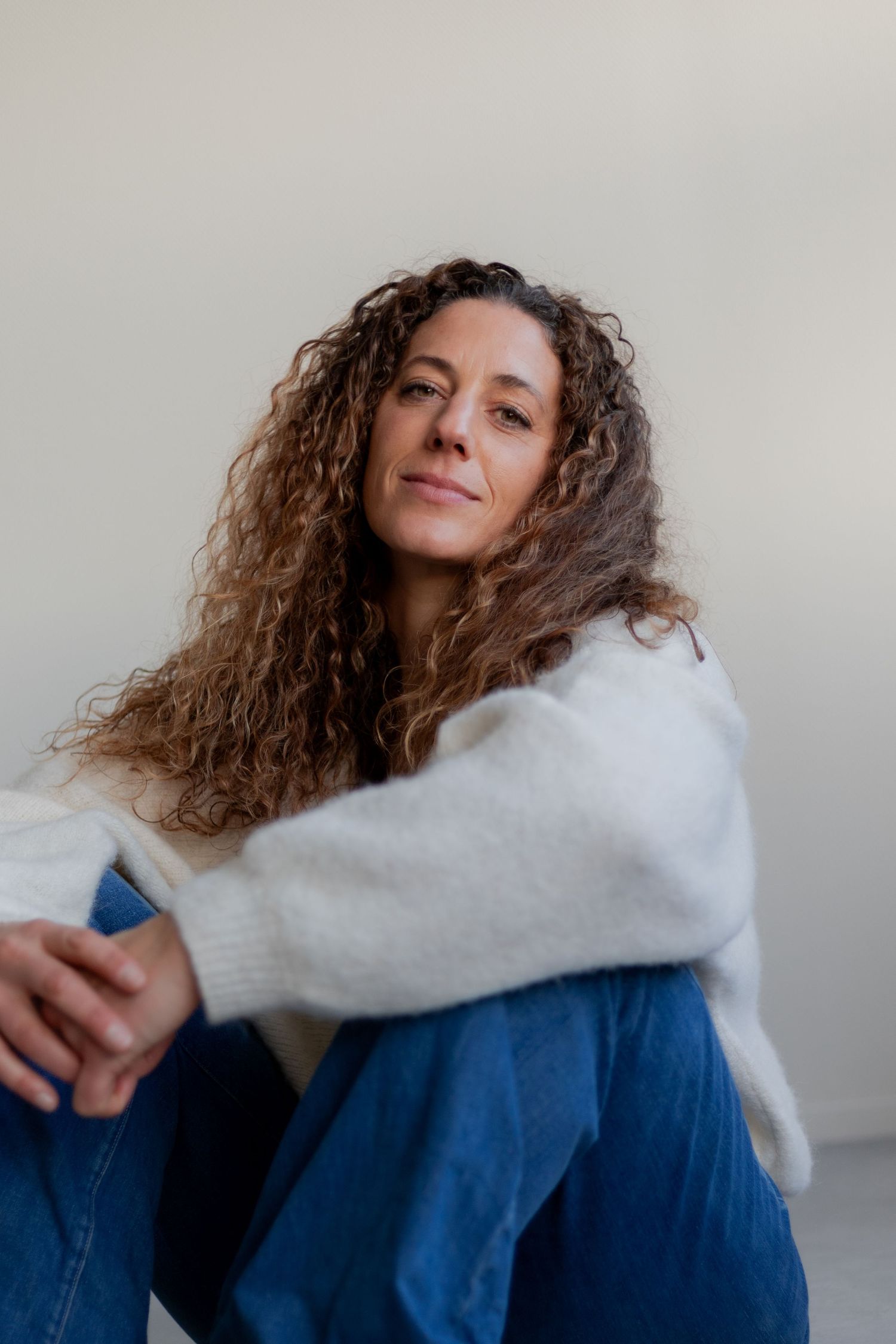 Person with curly hair wearing a white sweater and blue jeans poses against a light background in a series of shots.
